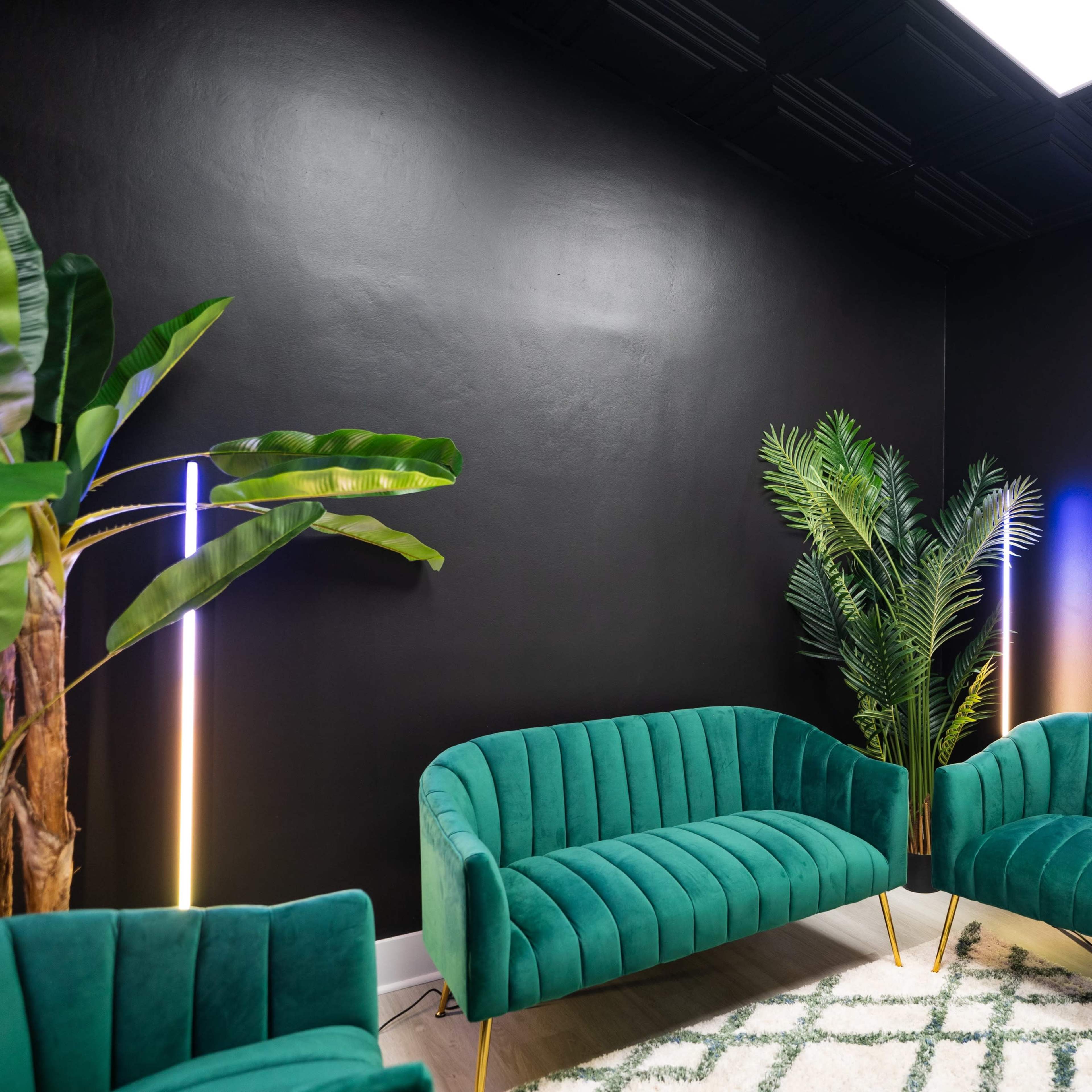 The room features two green velvet sofas, a large potted plant, neon "ON AIR" signage, and a dark wall with a textured ceiling.