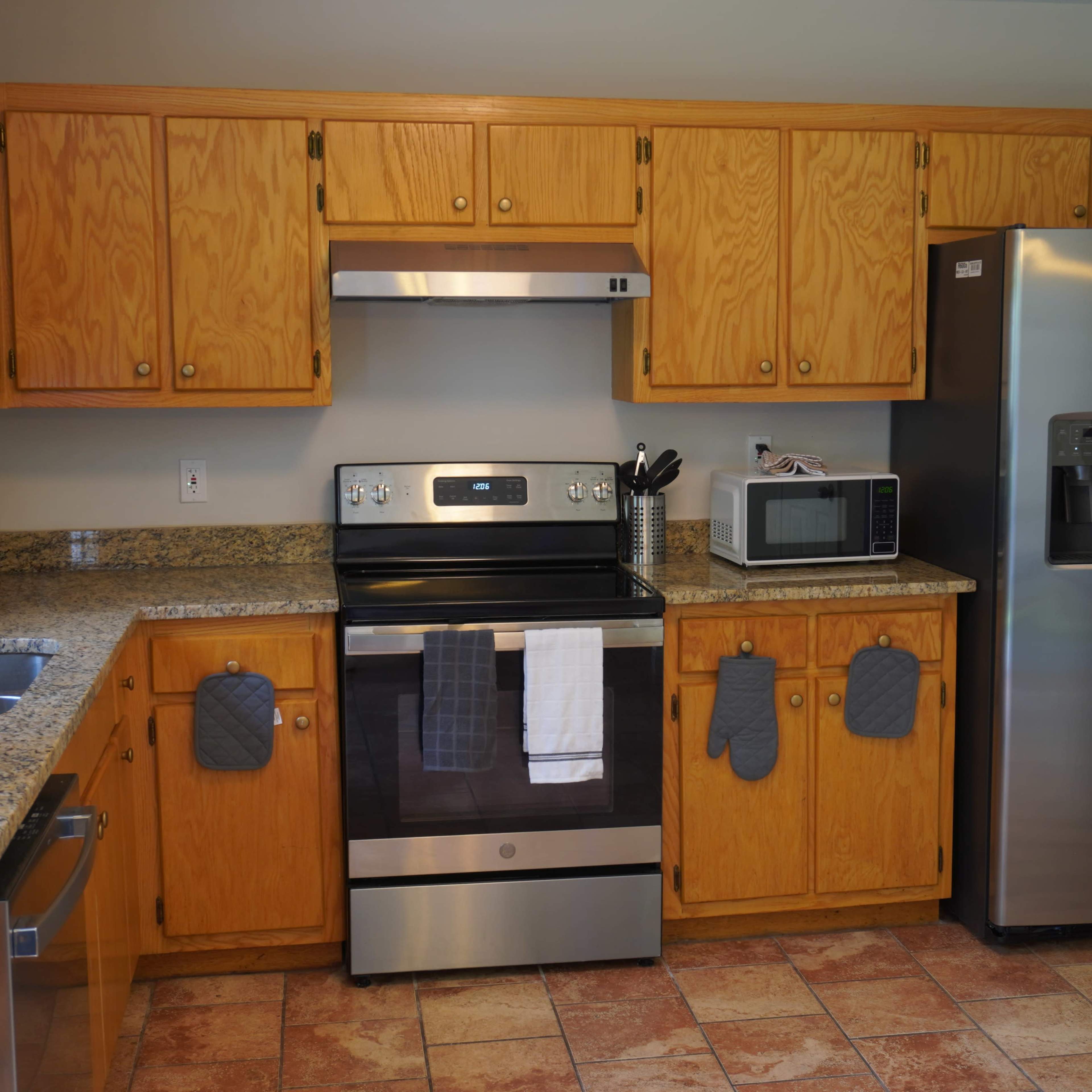 A kitchen with wooden cabinets, a stainless steel refrigerator, an oven, a microwave, and granite countertops.