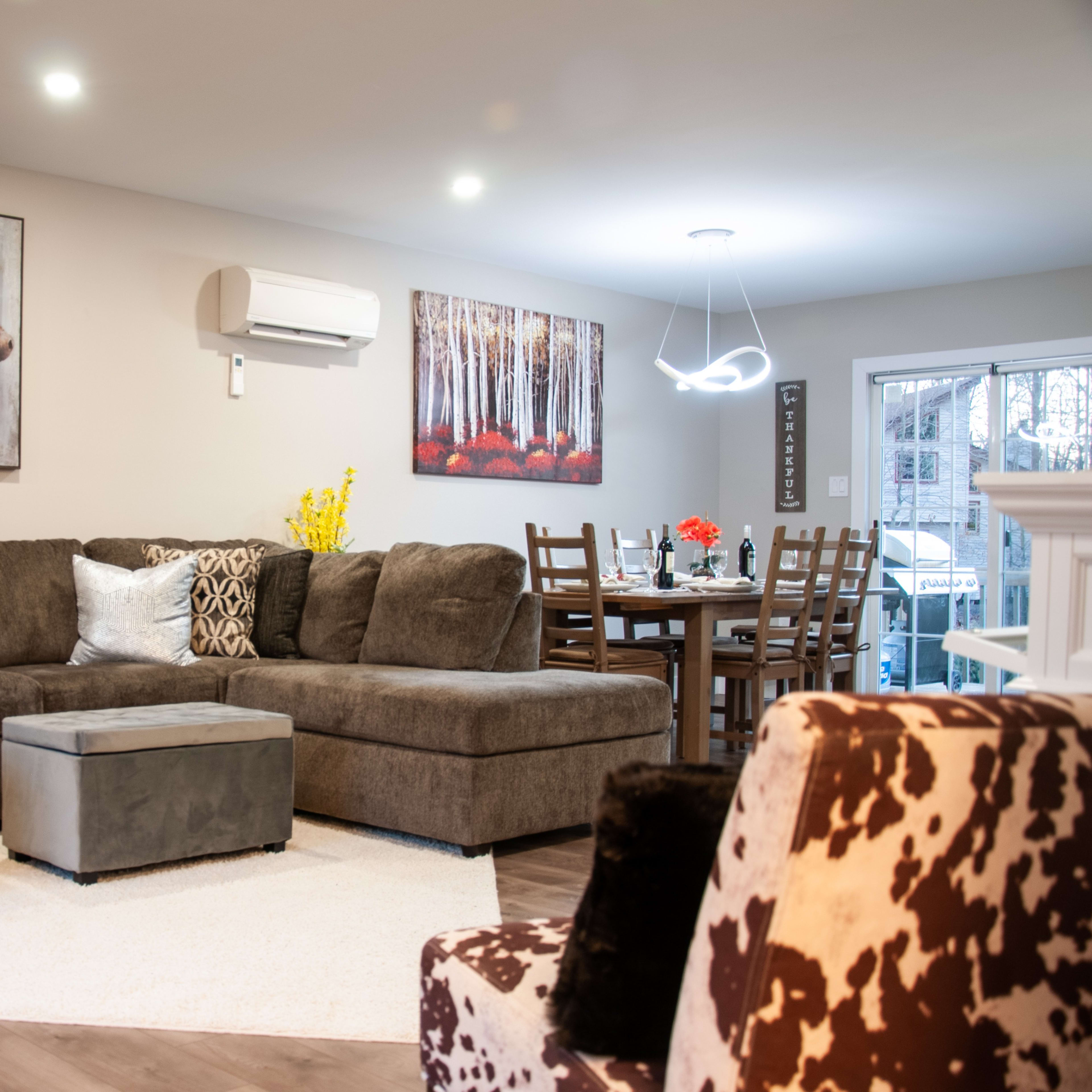 A spacious living room features a large sectional sofa, a coffee table, and artwork on the walls, with a dining area visible in the background.