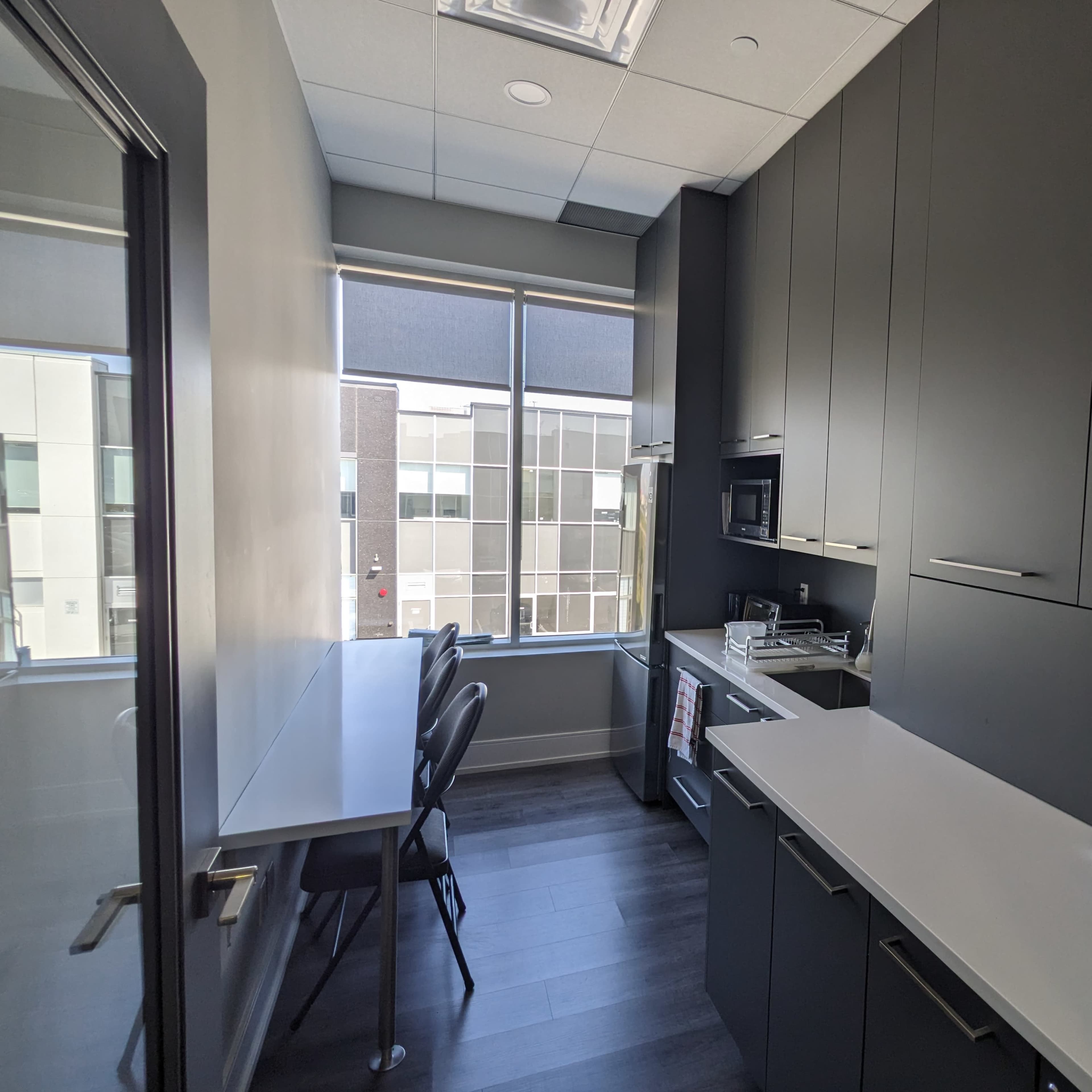 A modern kitchen with dark cabinets, a microwave, and a small table with chairs located near large windows.