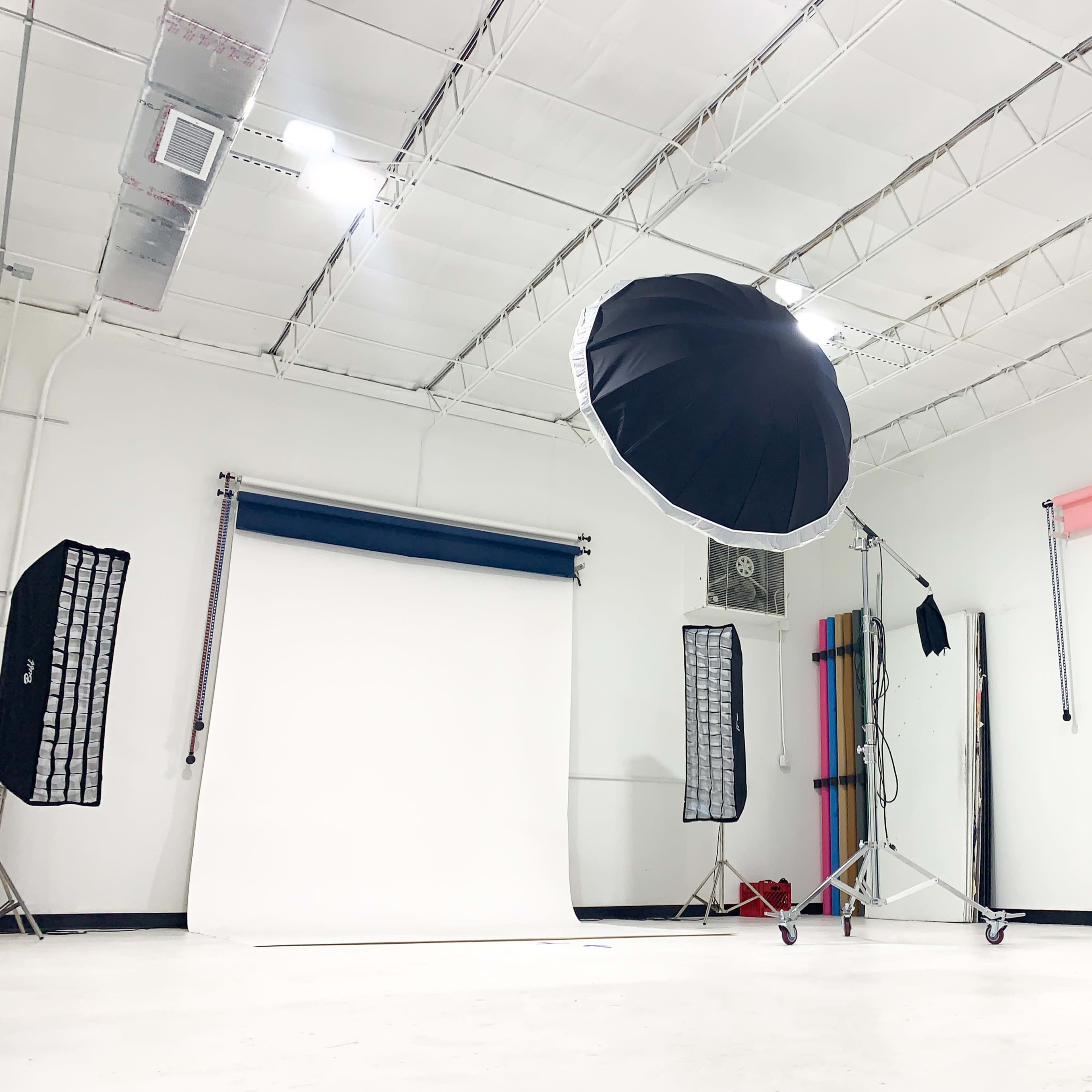 A photography studio with a large softbox light, two backdrop rolls, and various lighting equipment set up against white walls.