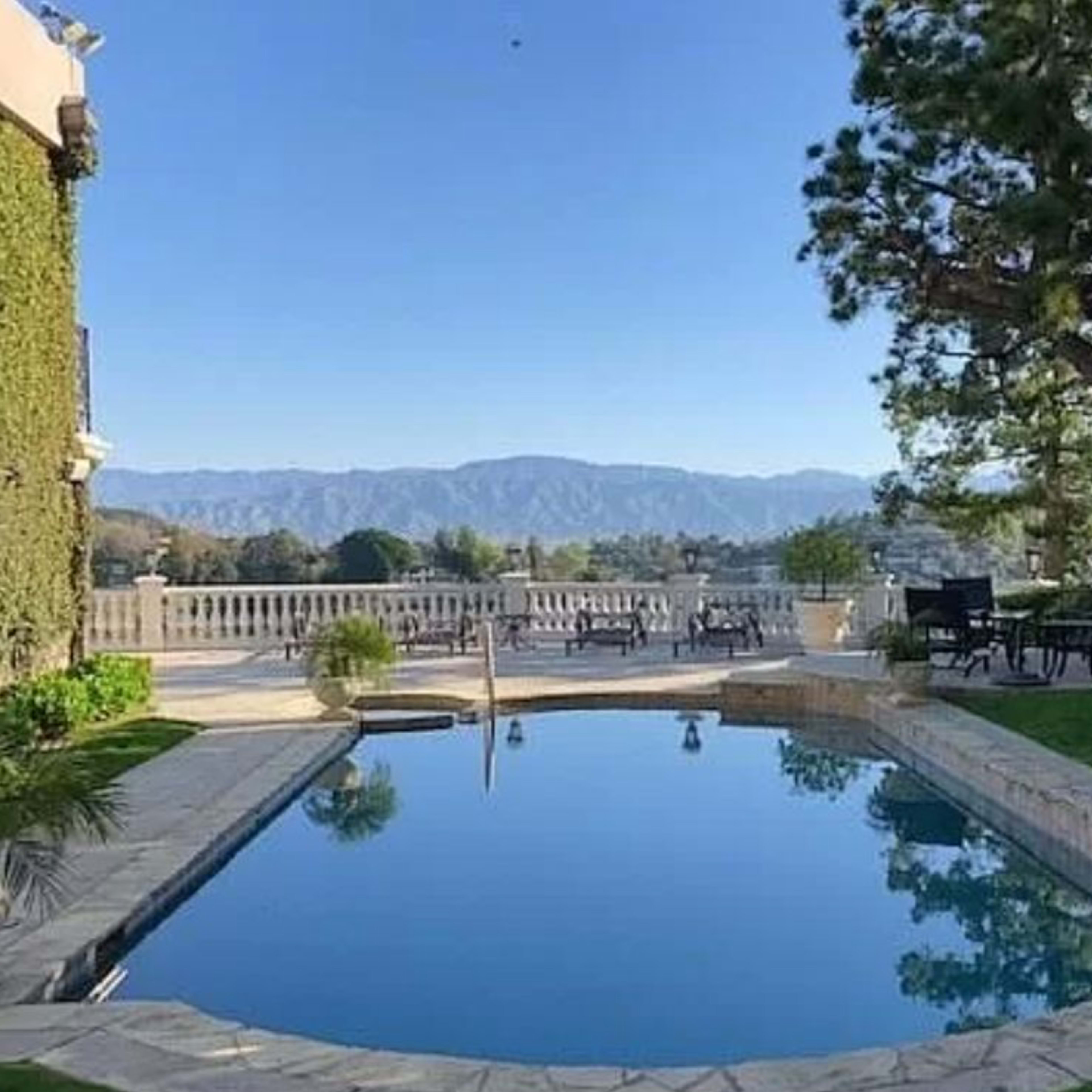 A swimming pool surrounded by greenery and mountains in the background.