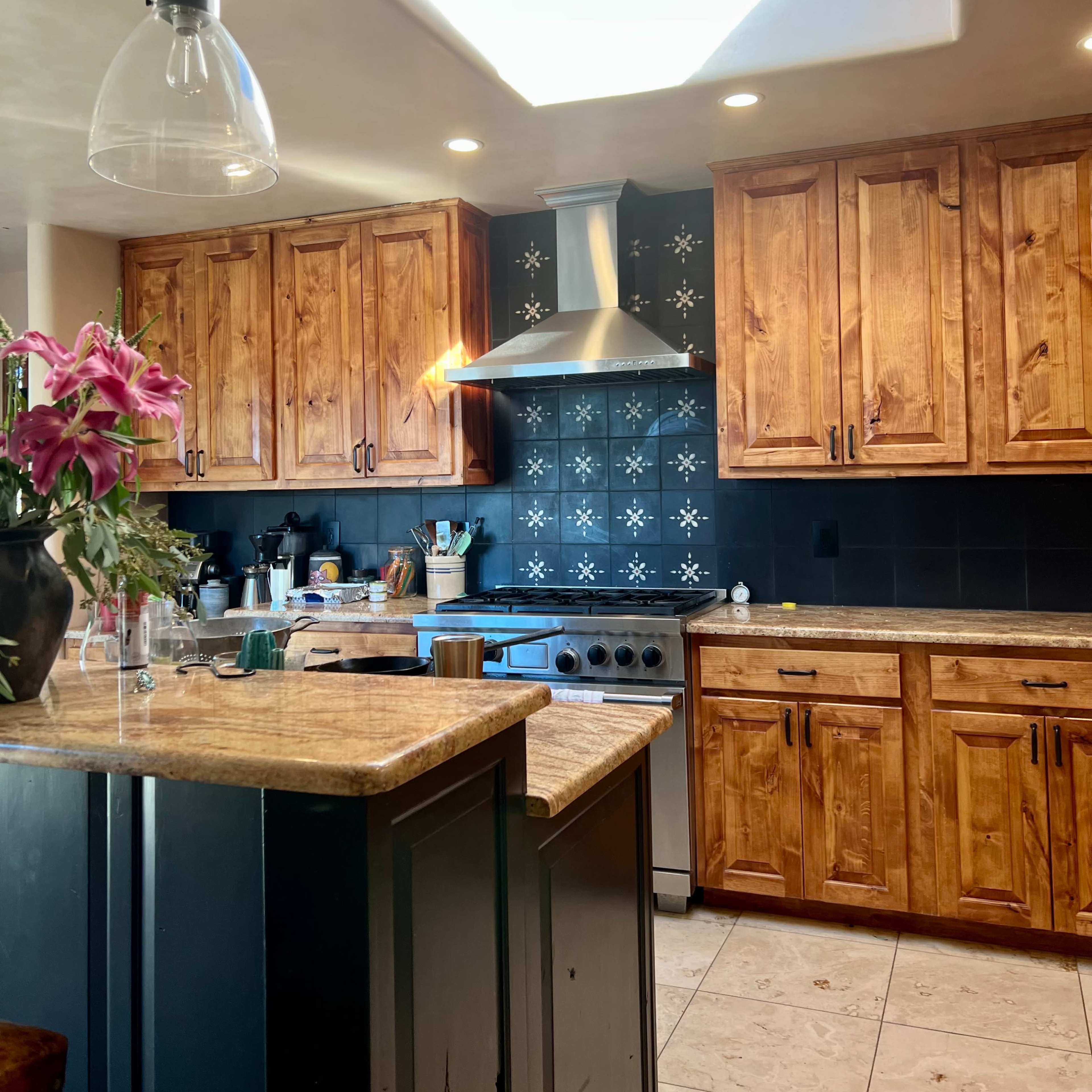 A modern kitchen features wooden cabinets, a stainless steel range hood, and a skylight illuminating the space.