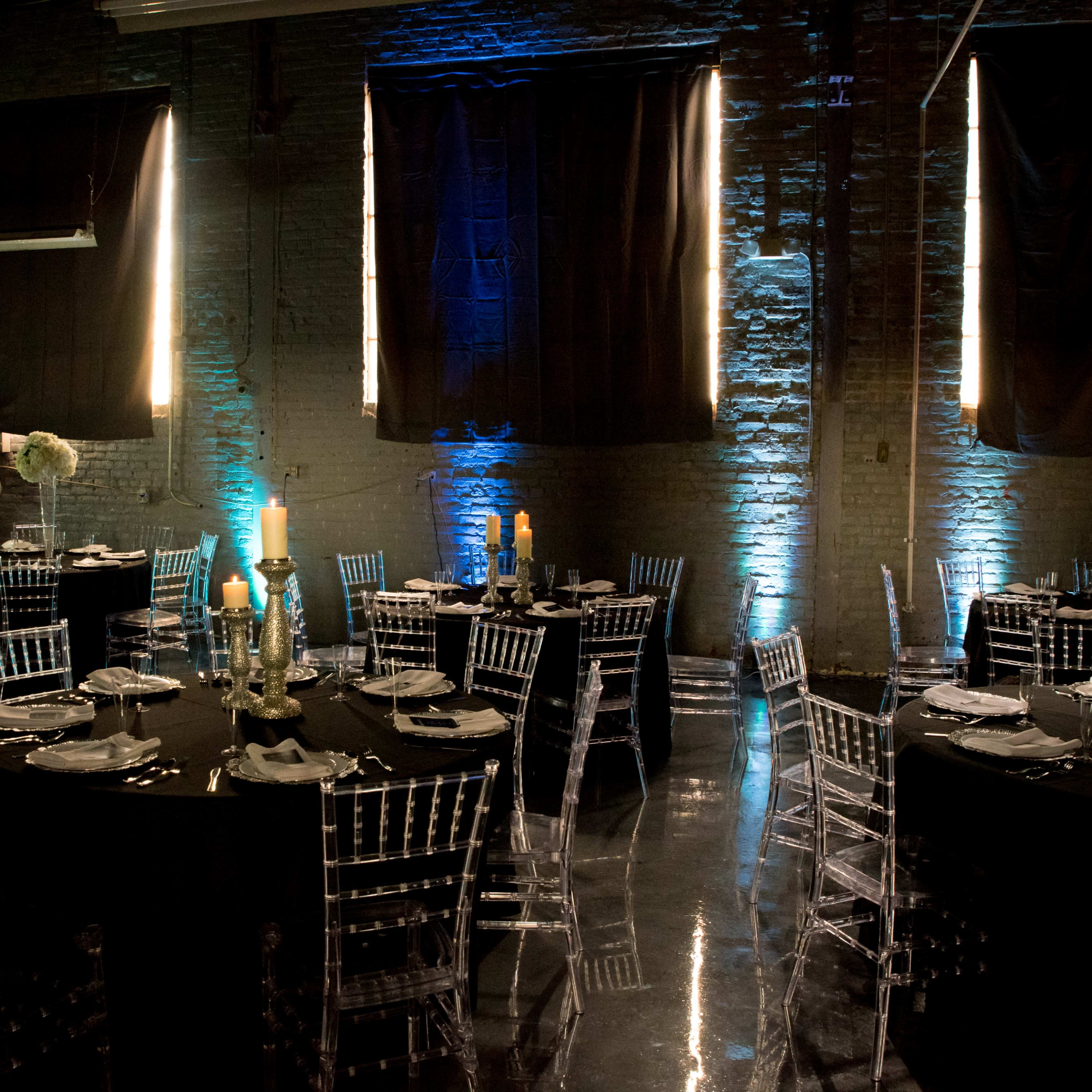 The scene features a banquet hall set for a celebration, with round tables covered in black cloth, clear Chiavari chairs, and illuminated number displays reading "65."