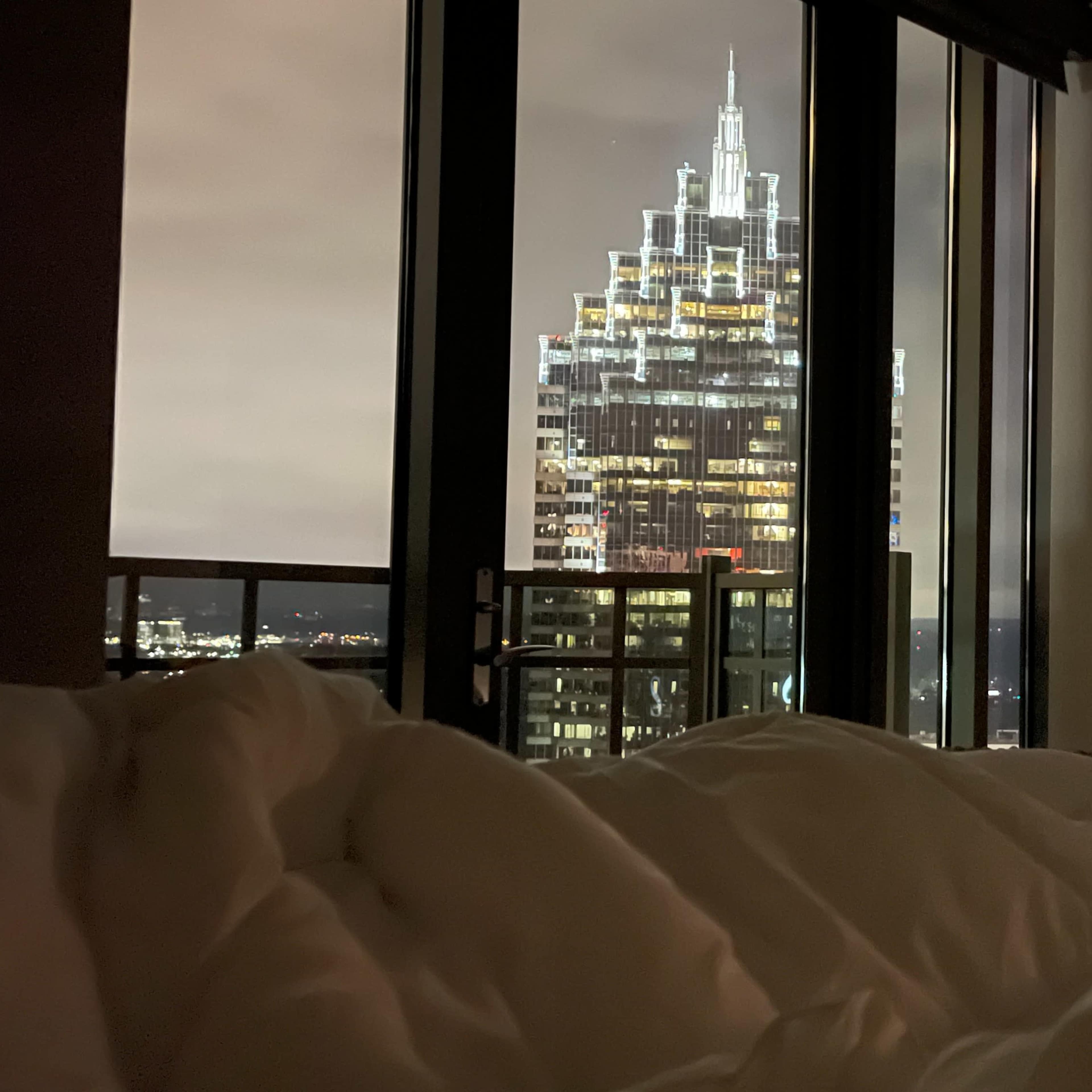 A view from a bedroom showing a city skyline with a prominent, lit building in the background.
