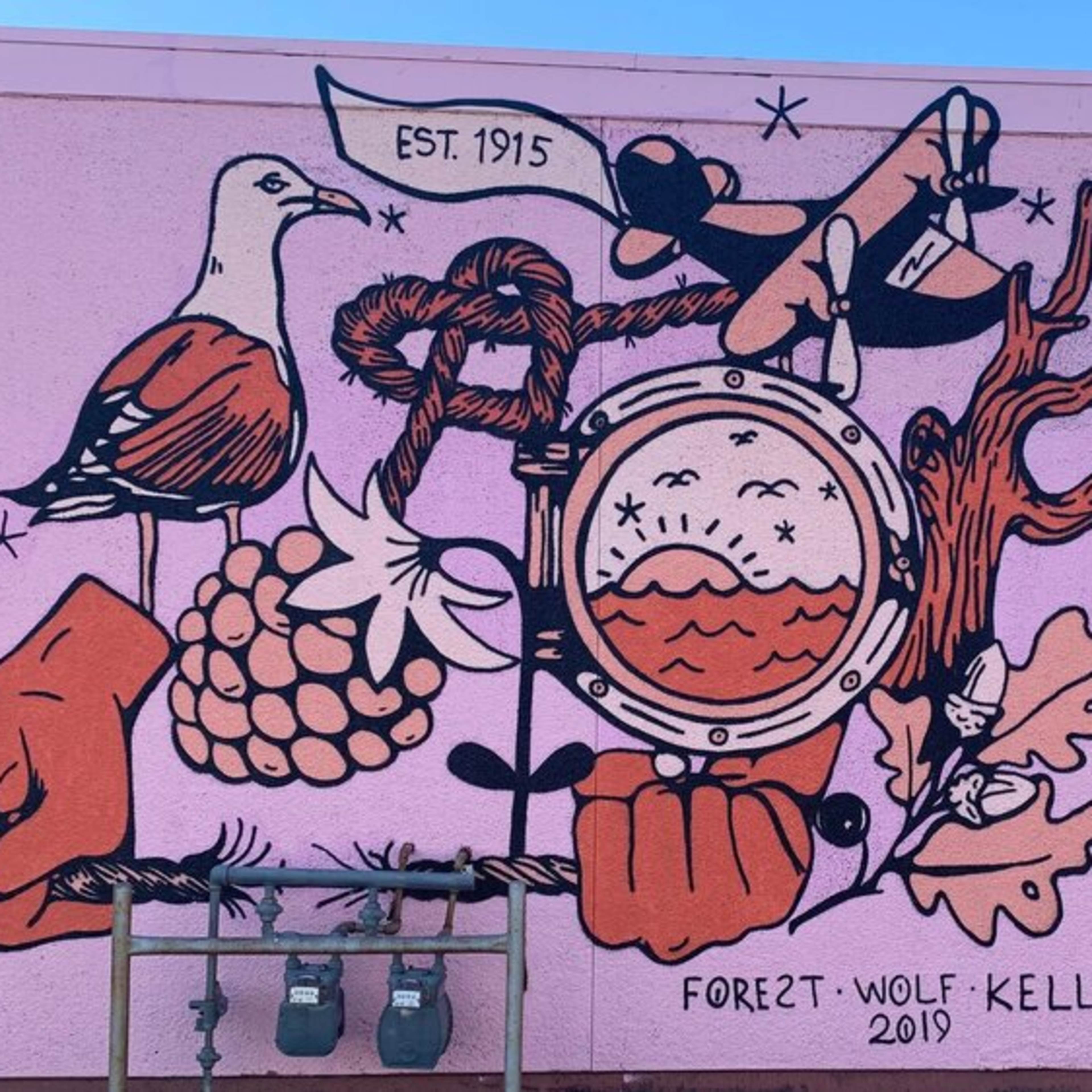 A colorful mural depicting various elements such as birds, grapes, and hands, along with a compass and scales, all intertwined with abstract shapes against a pink background.