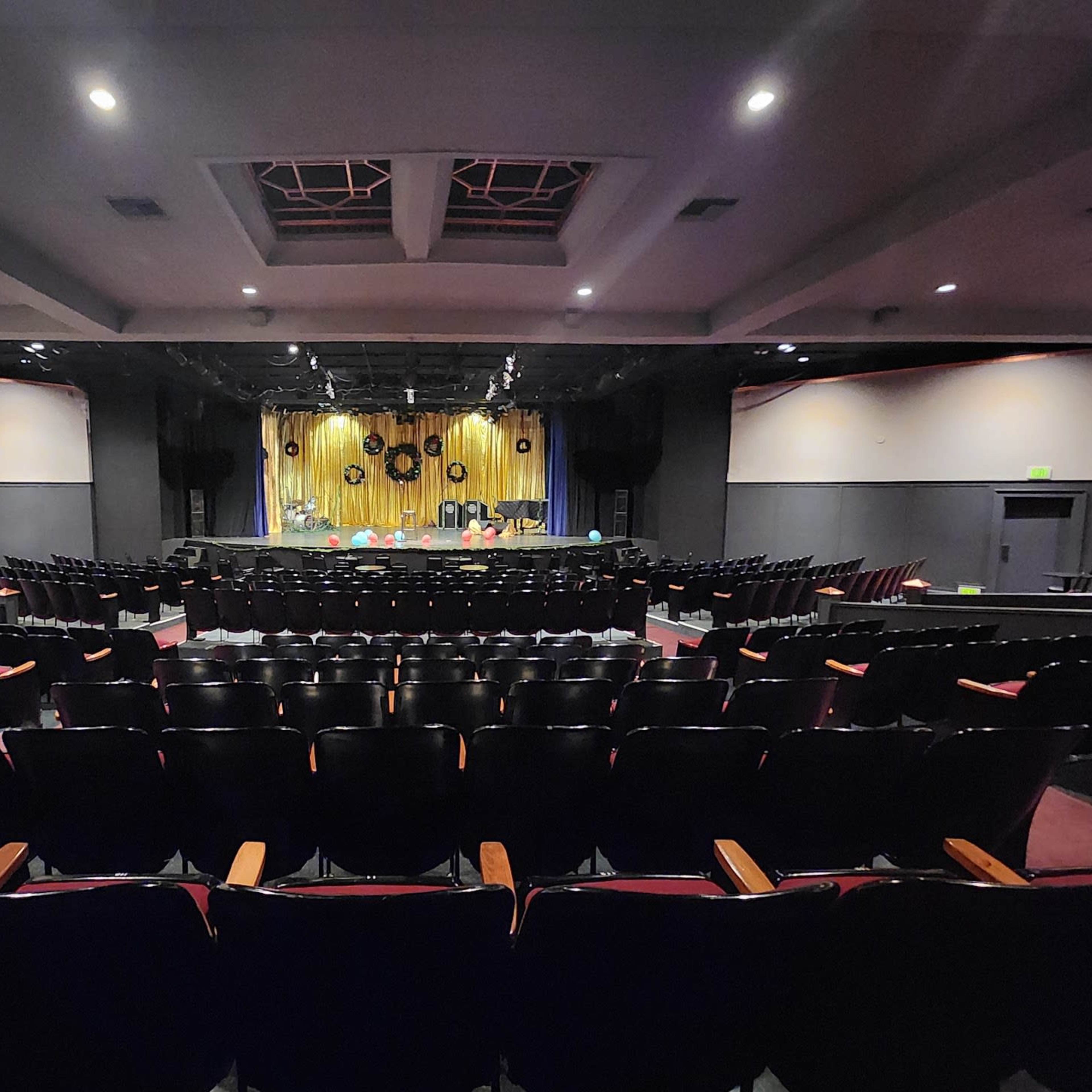 A darkened theater with rows of empty black seats facing a stage adorned with yellow curtains and decorative elements.