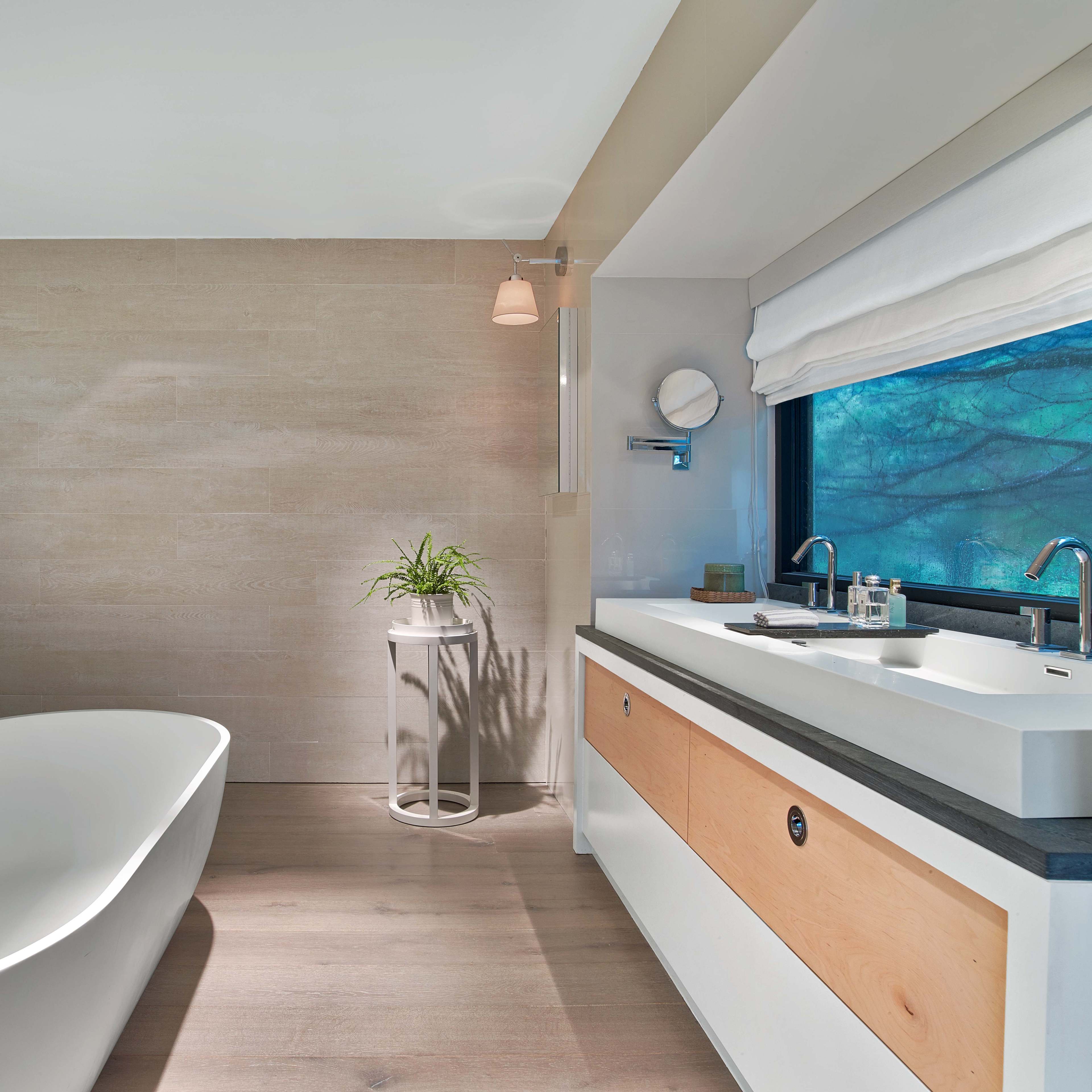 A modern bathroom with a freestanding bathtub, a sleek vanity with a sink, and a window overlooking greenery.