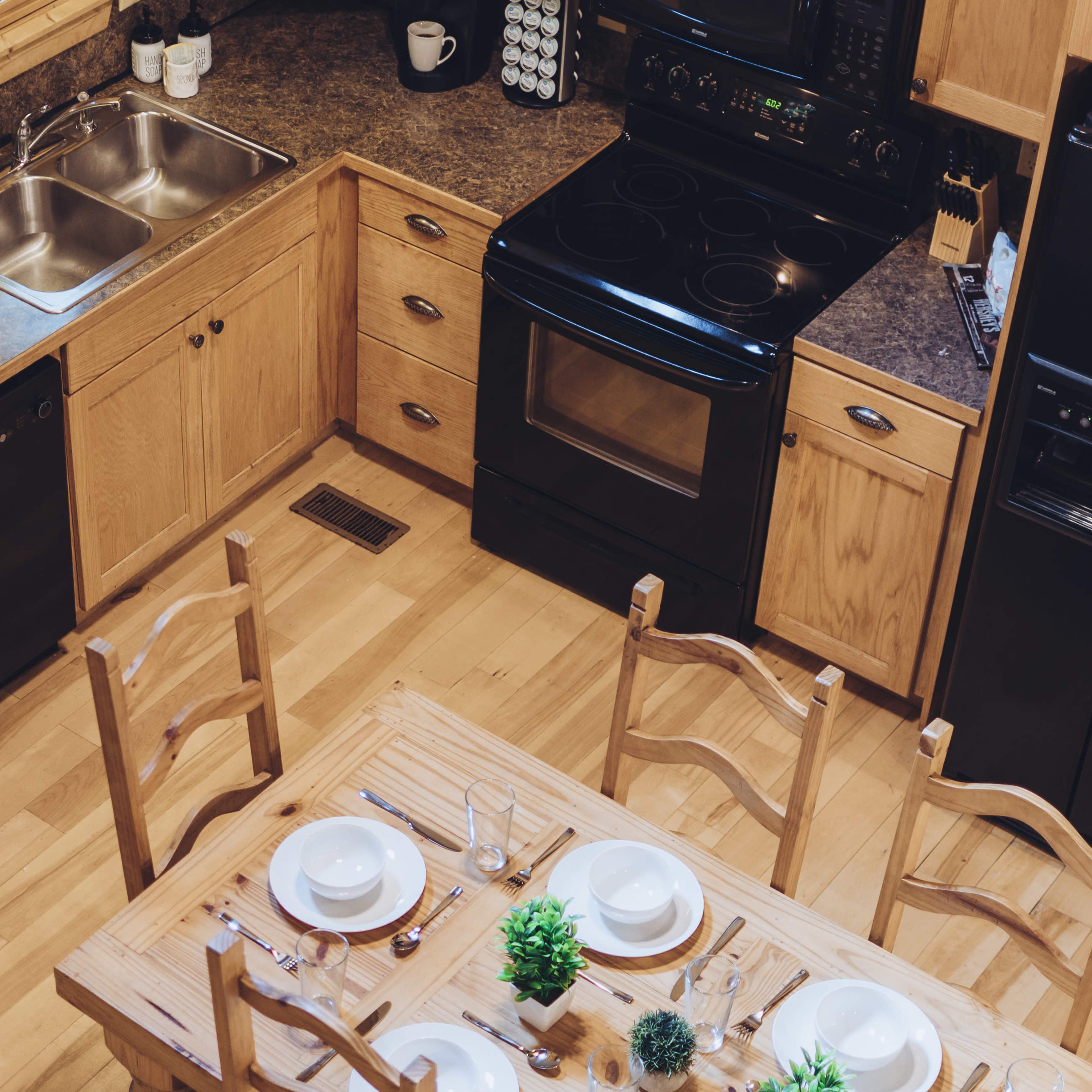 A well-organized kitchen features wooden cabinets, a black stove and dishwasher, a double sink, and a dining table set for a meal.