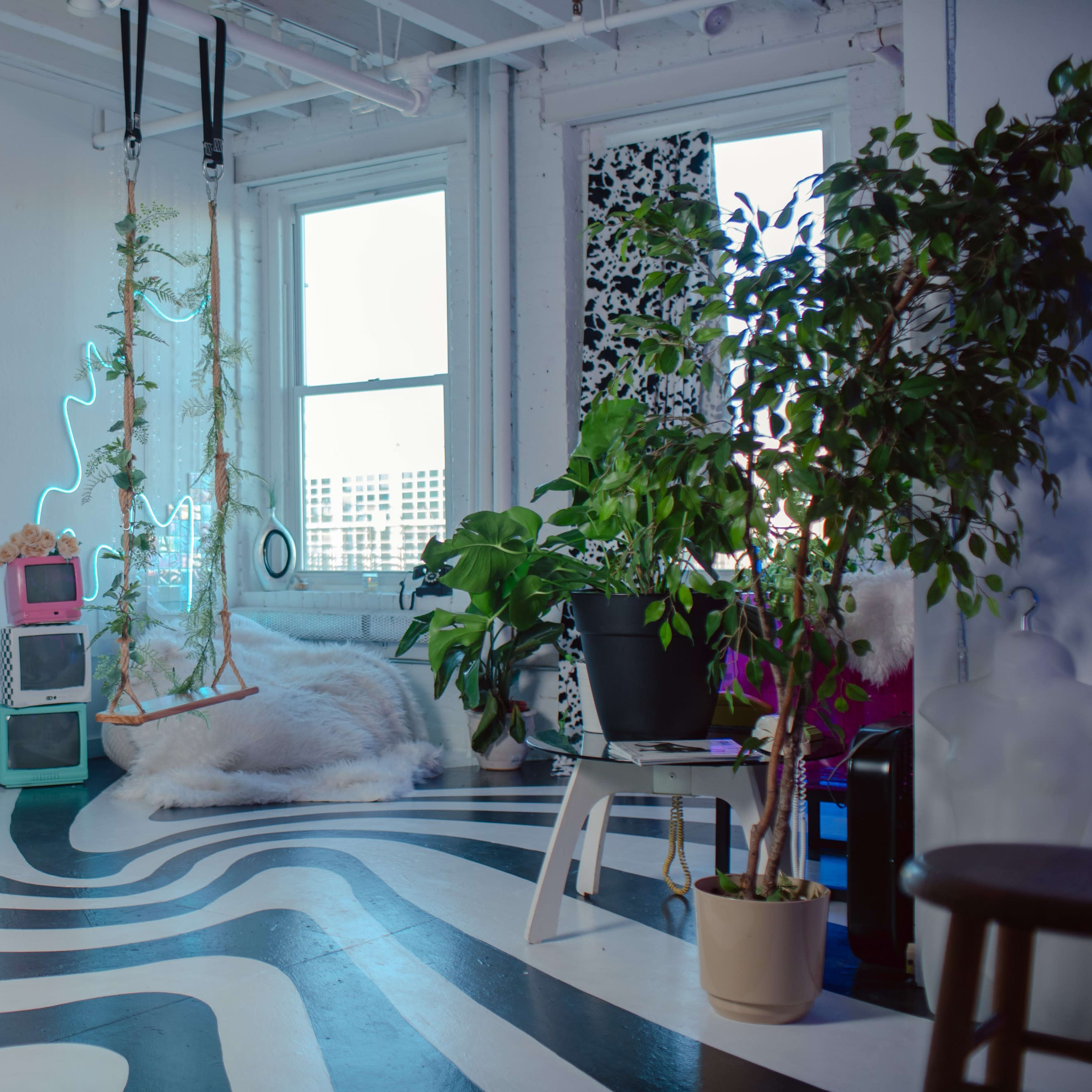 A modern, minimalist interior space with a patterned floor, large windows, a swing, neon lights, and various plants.