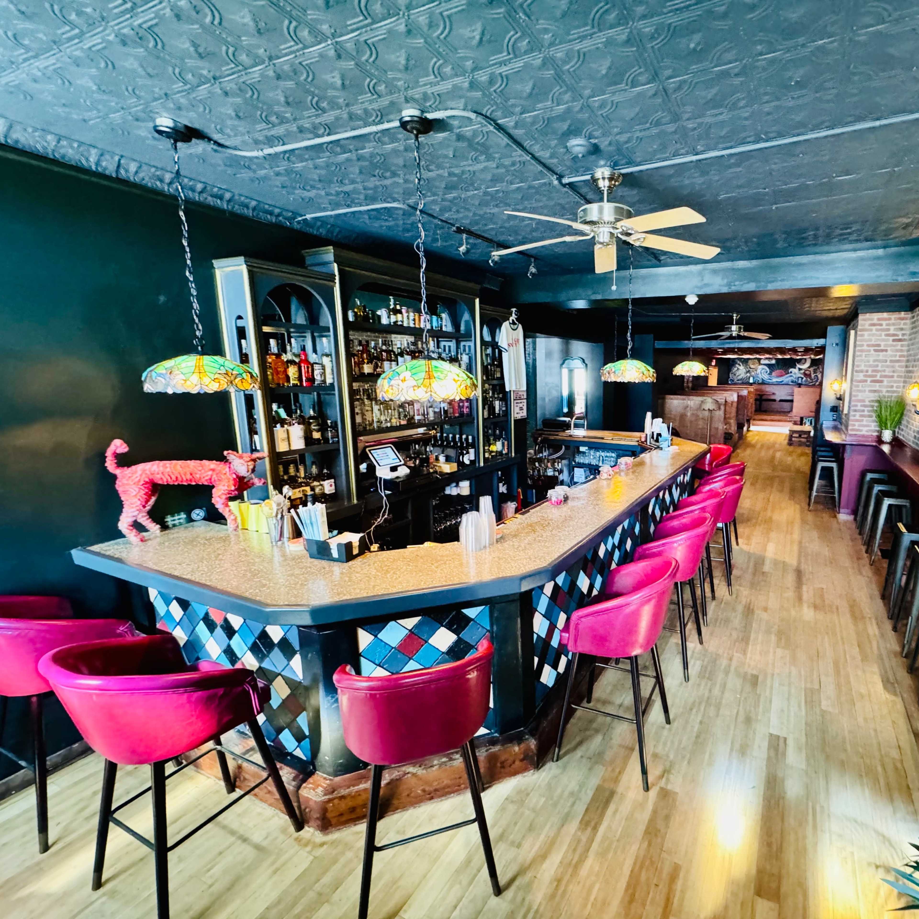 A bar interior with a colorful tiled counter, decorative lighting, and a variety of seating options along the walls.