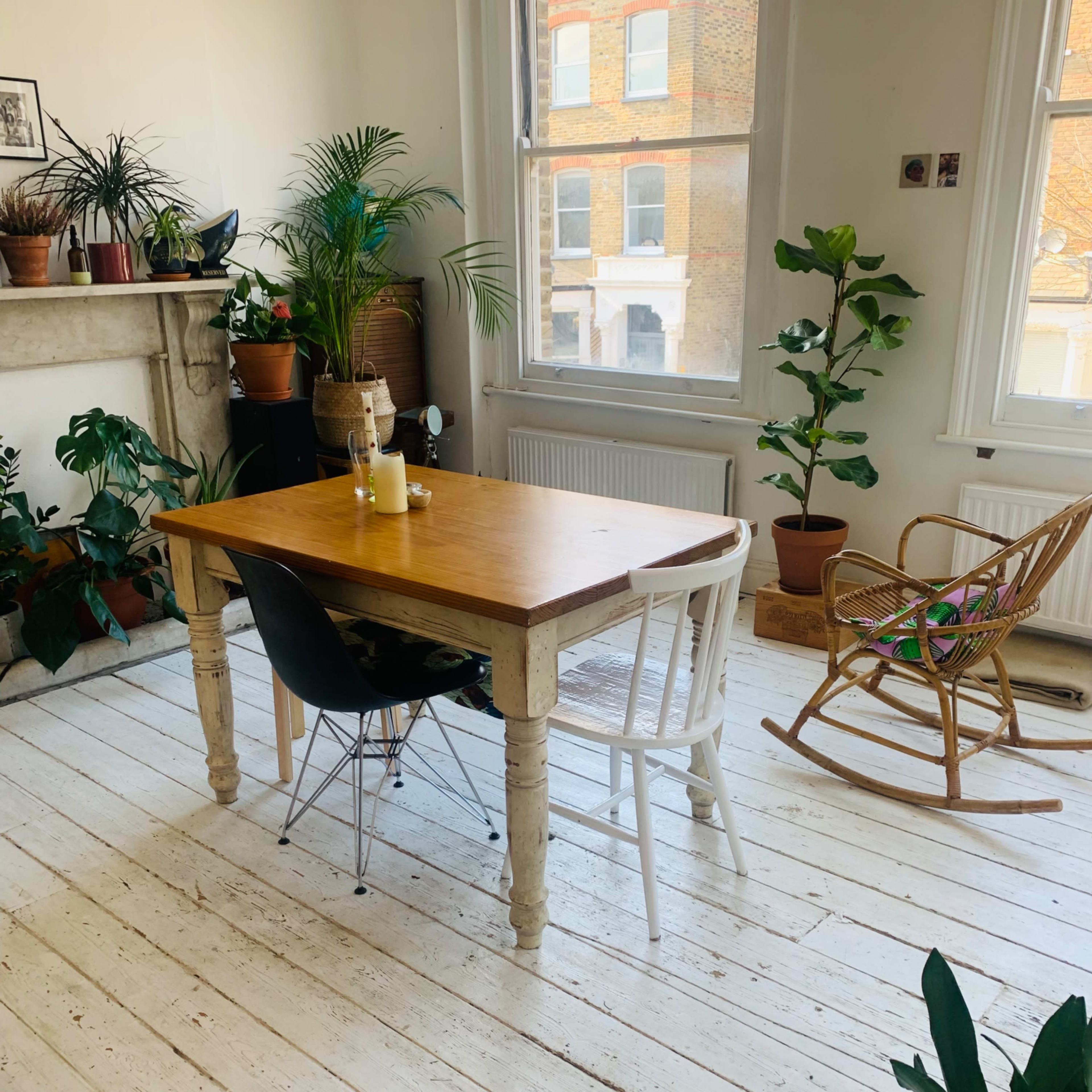 A wooden table with a black chair and a white chair sits by a window in a room filled with various potted plants.