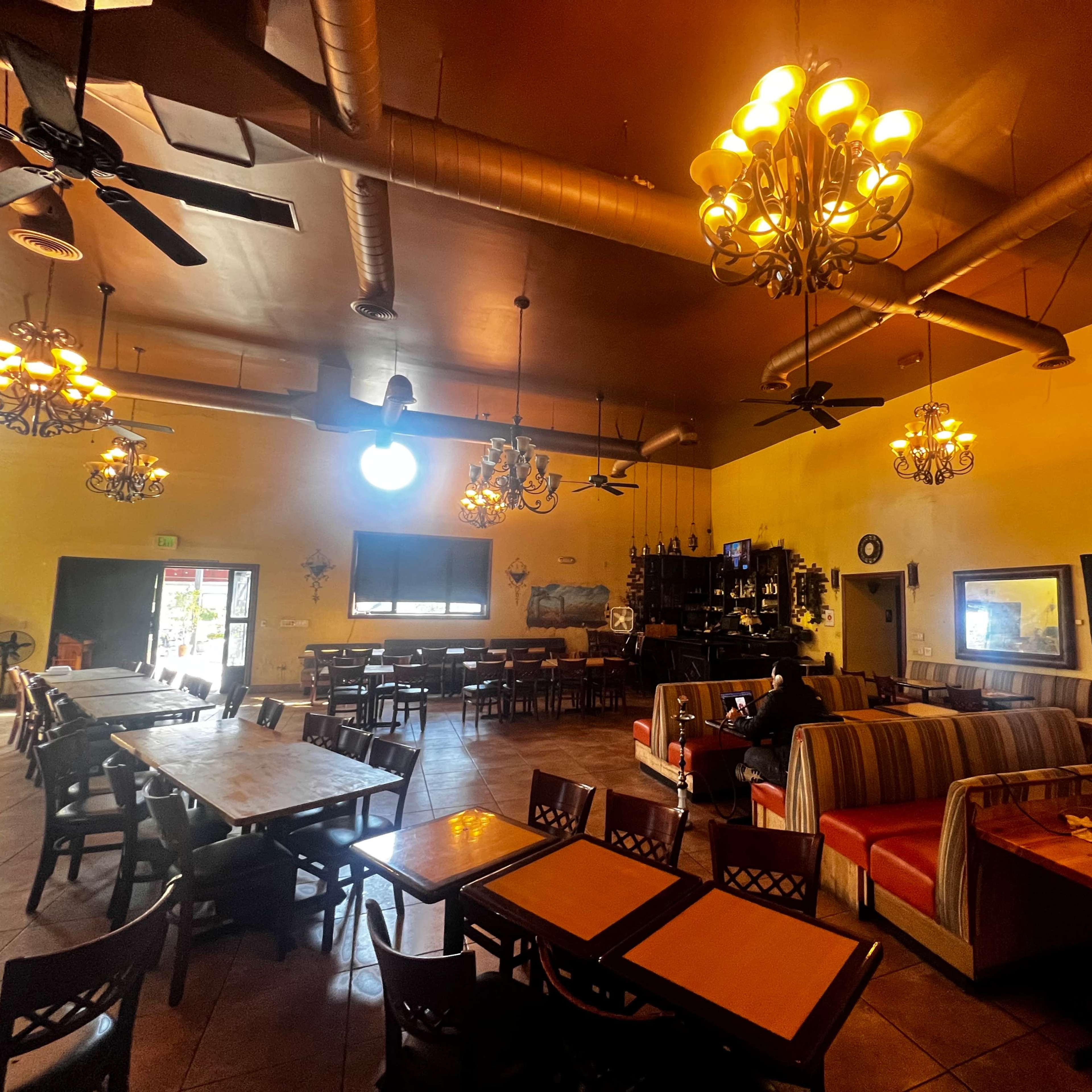 A spacious restaurant interior with wooden tables, chairs, and ceiling fans, illuminated by several chandeliers.