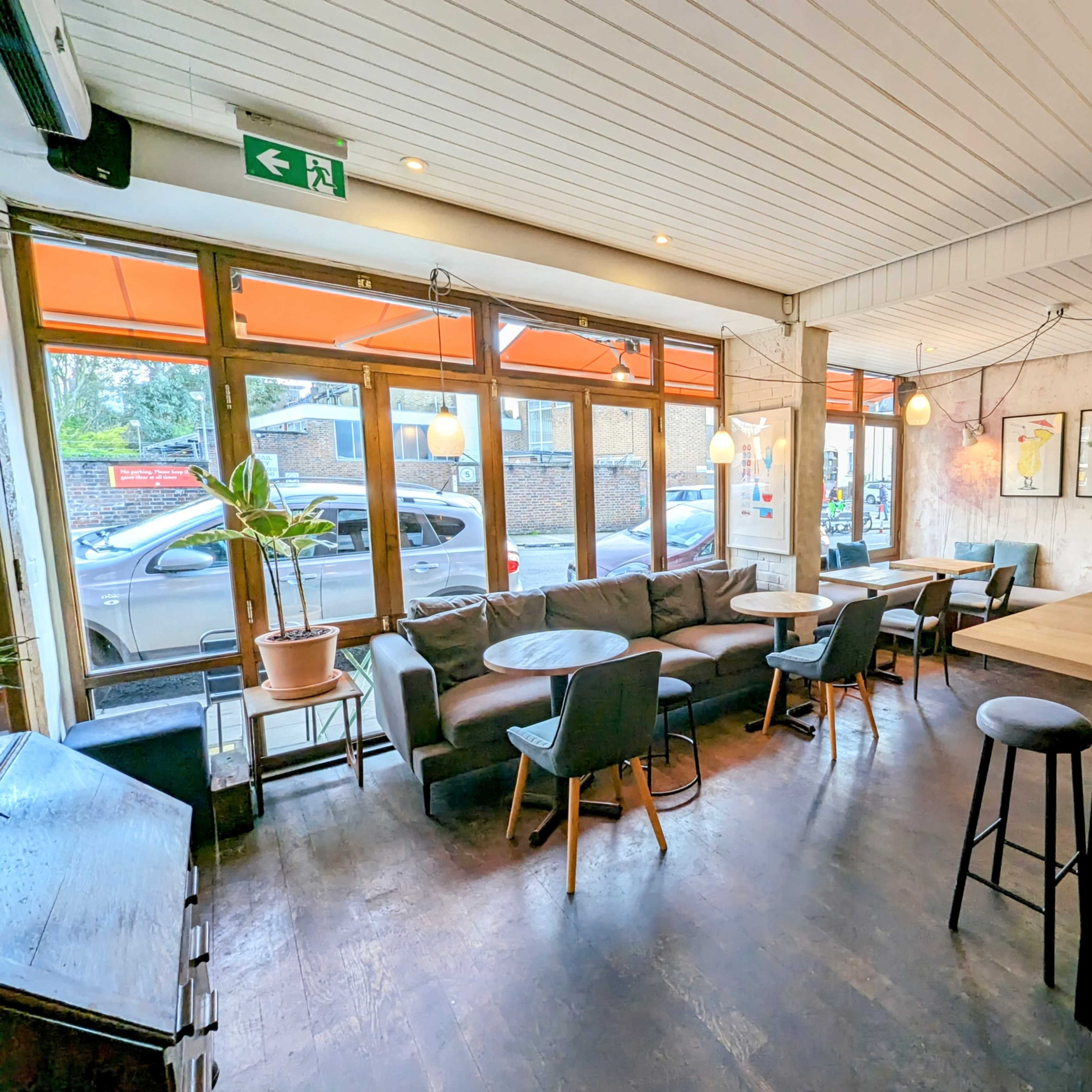 A cozy café interior with seating areas, large windows, and a view of parked cars outside.