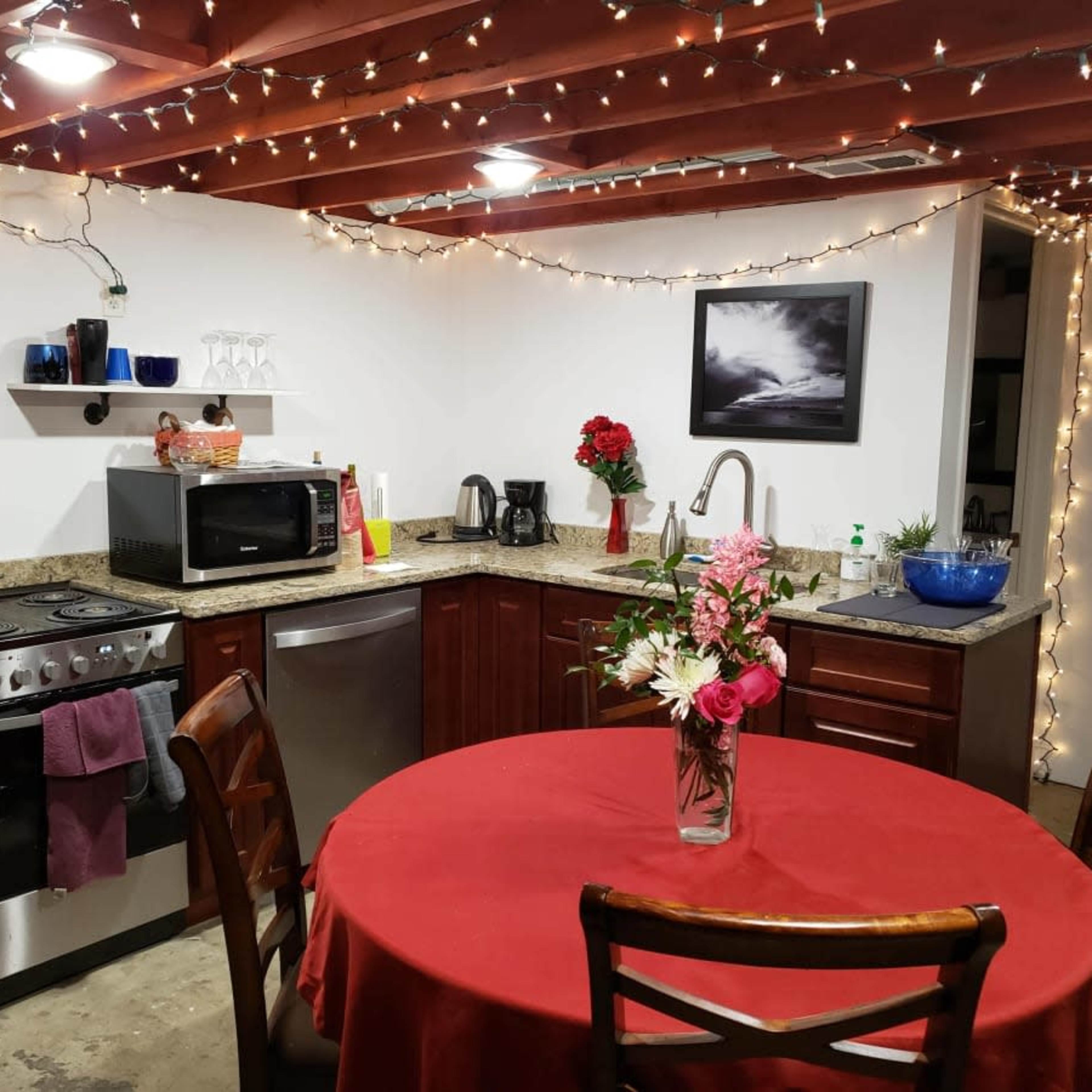 A kitchen with wooden cabinets, a round table covered by a red tablecloth, and string lights illuminating the space.