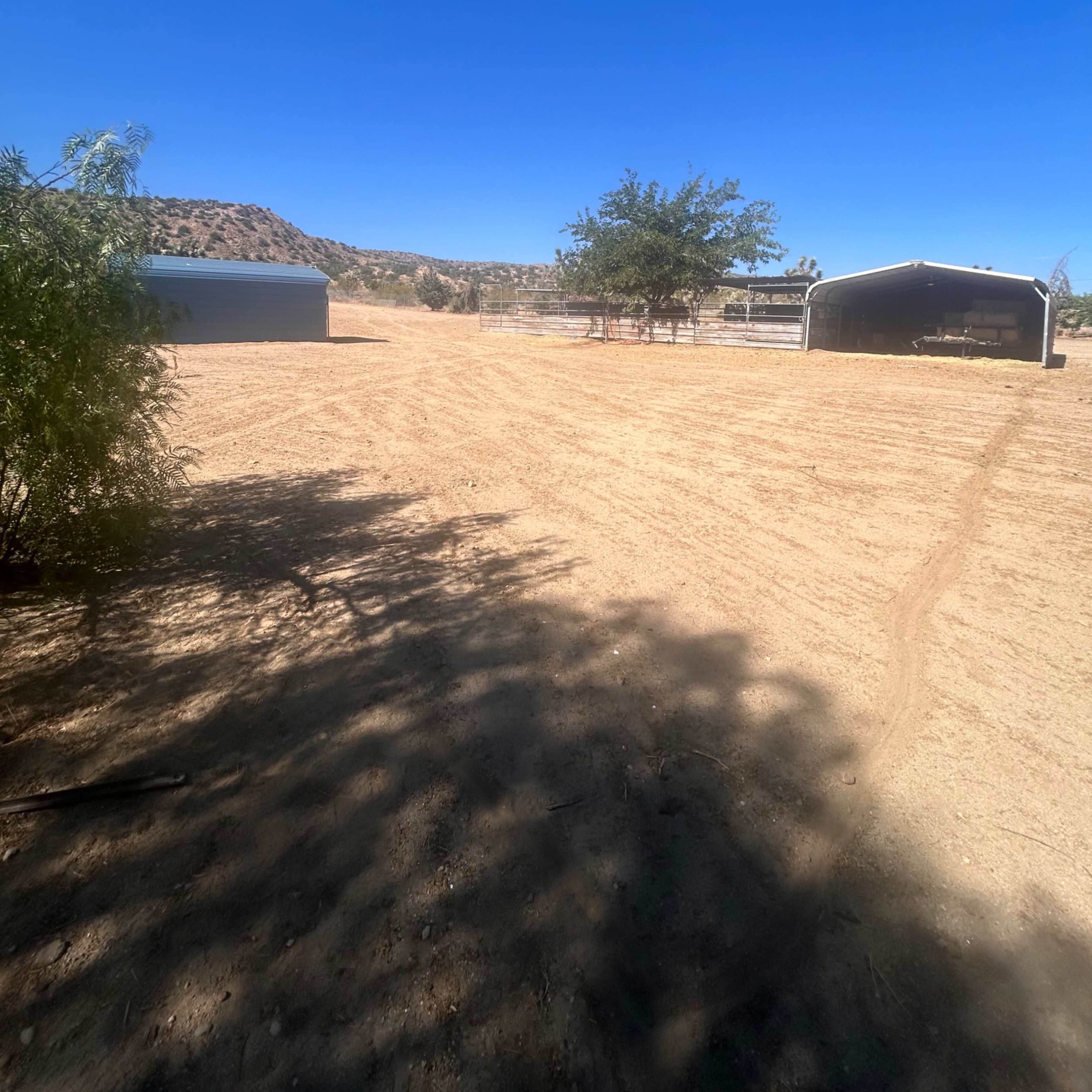 A sunlit, bare landscape with two metal structures and sparse vegetation against a clear blue sky.