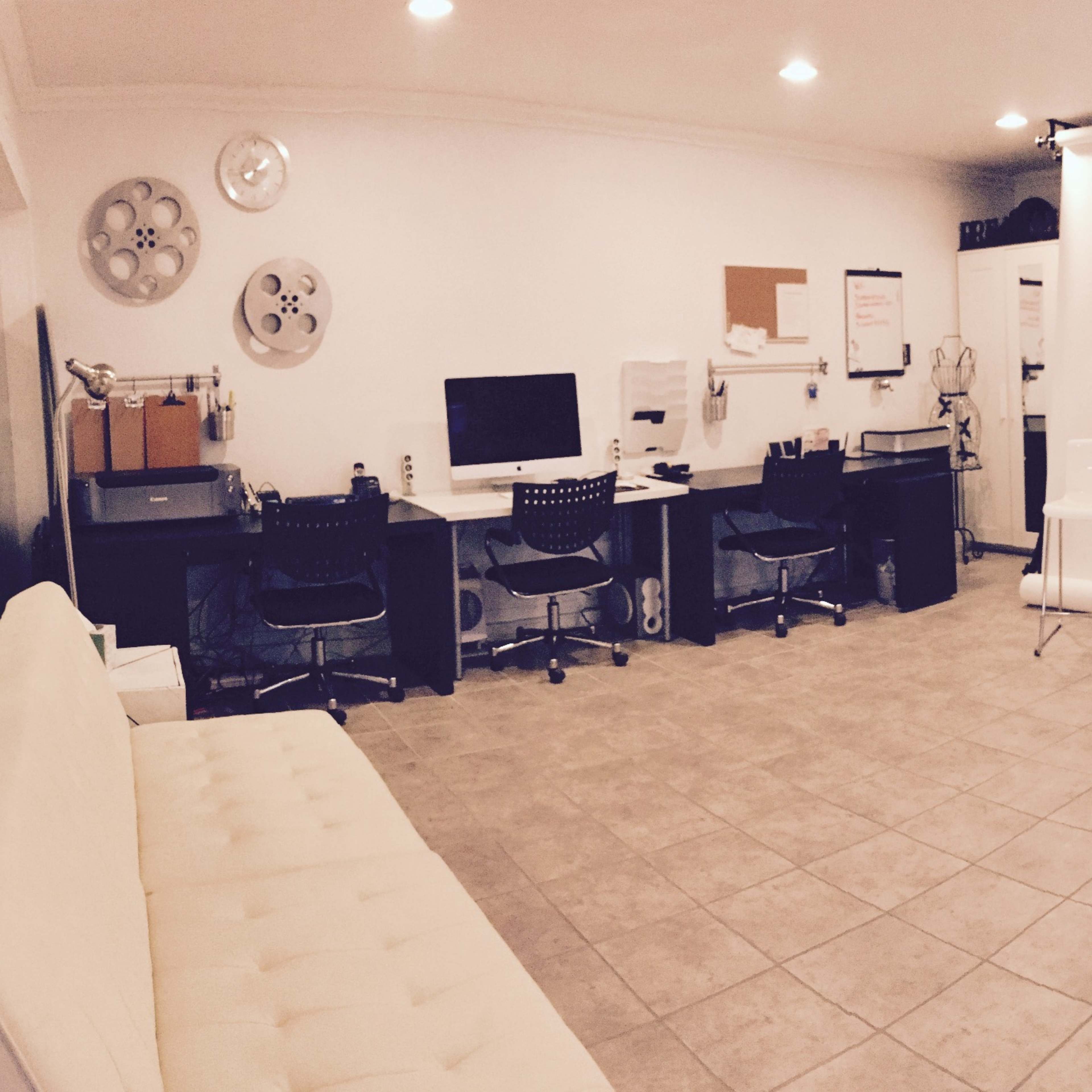 A photography studio with a white backdrop, a seating area, and workstations containing computers and other equipment.