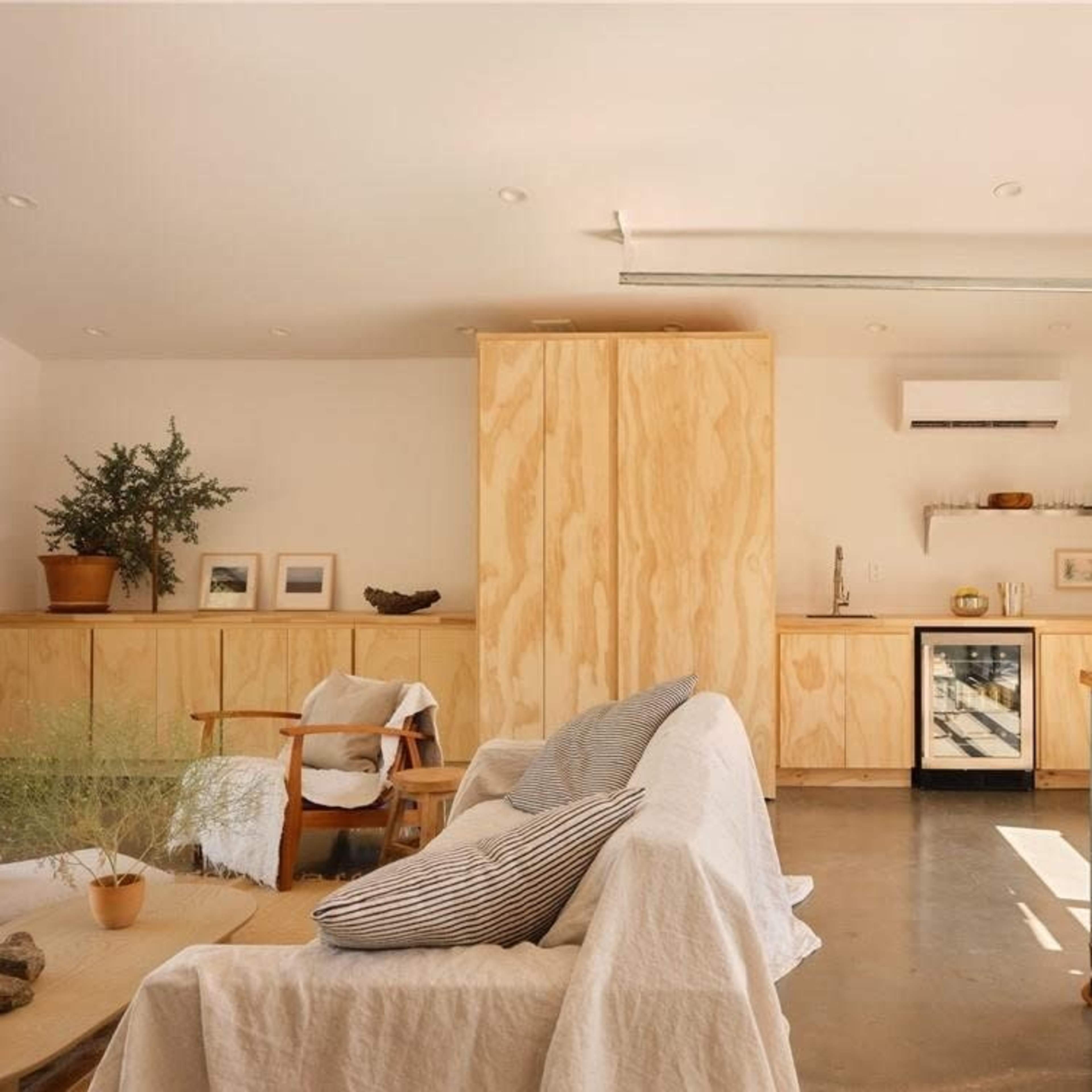A modern living space with wooden cabinetry, a small kitchen area, a seating arrangement, and large windows allowing natural light.