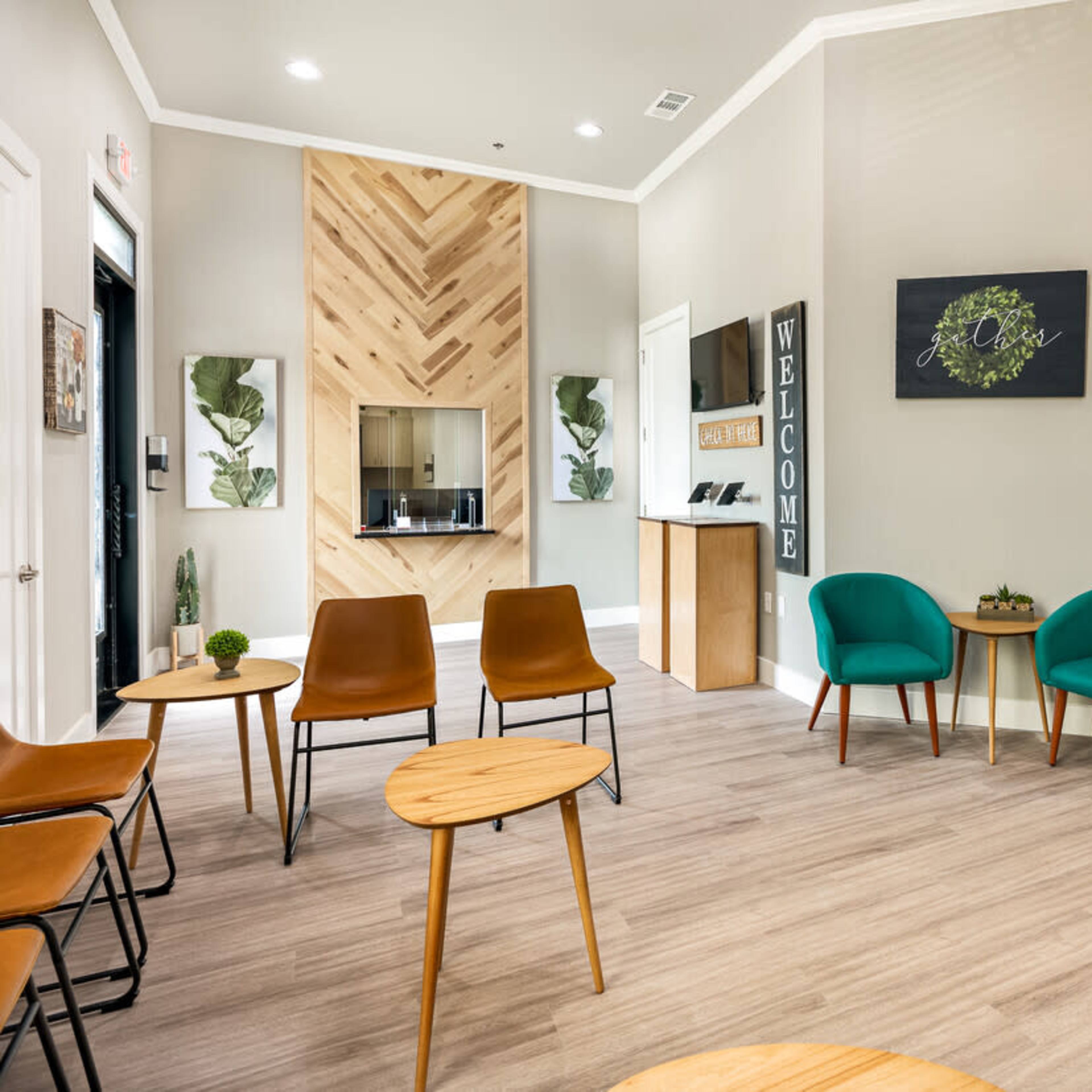 A modern waiting area with brown and teal chairs, small wooden tables, and a decorative wall with a welcoming sign.