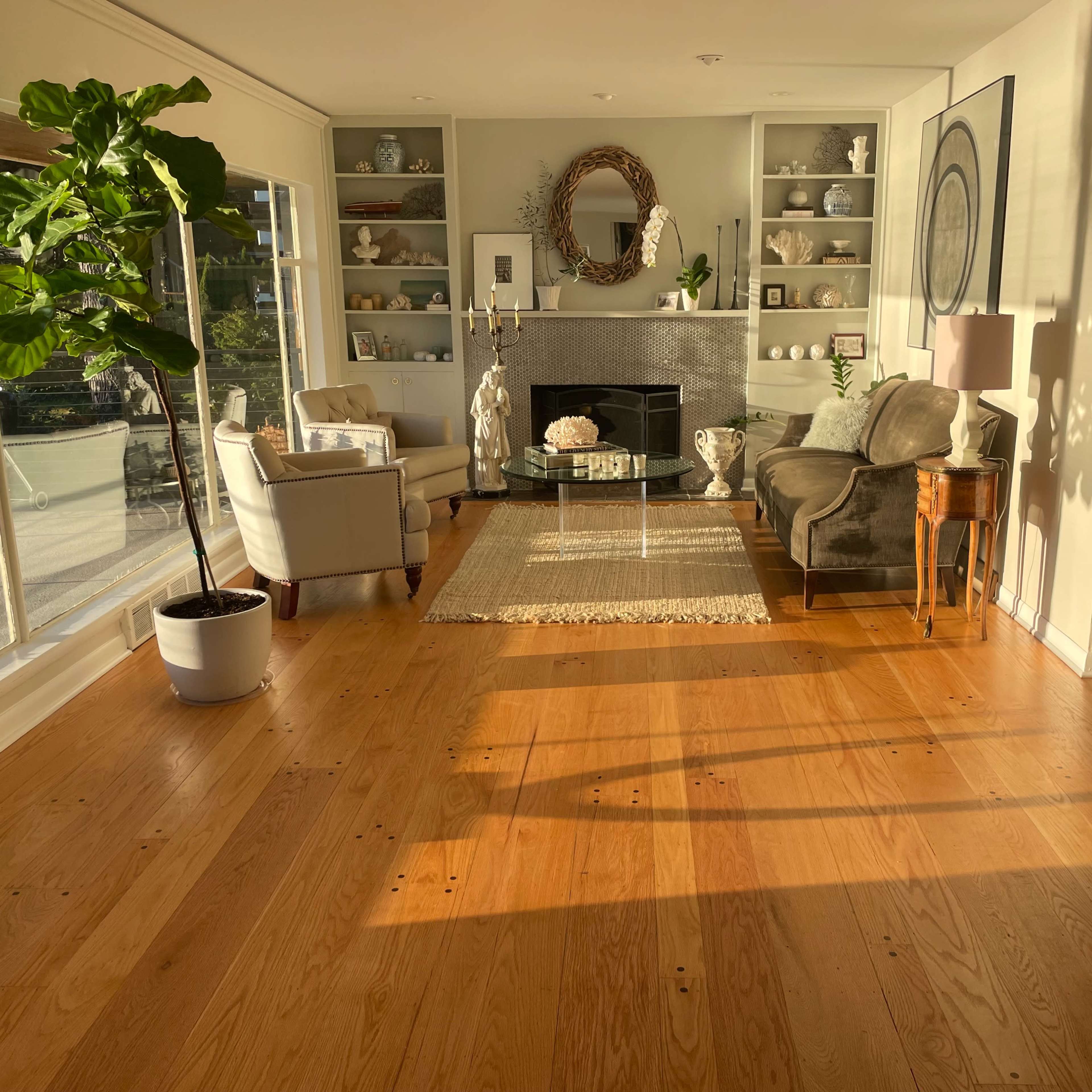 A bright living room features hardwood floors, a large window allowing natural light, a fireplace, and comfortable seating arrangements.