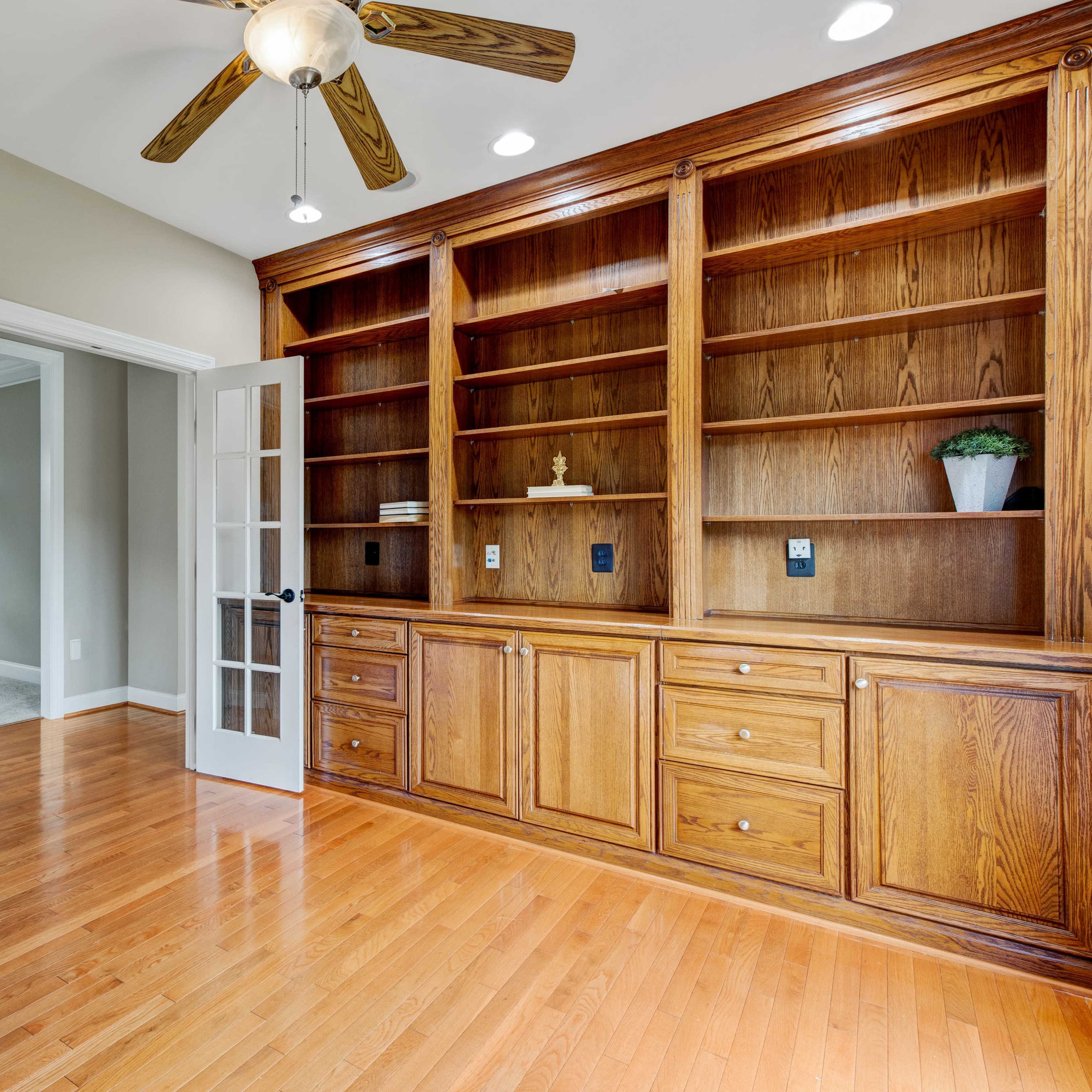 A well-lit room featuring a wooden shelving unit and double glass doors, with polished wooden flooring.