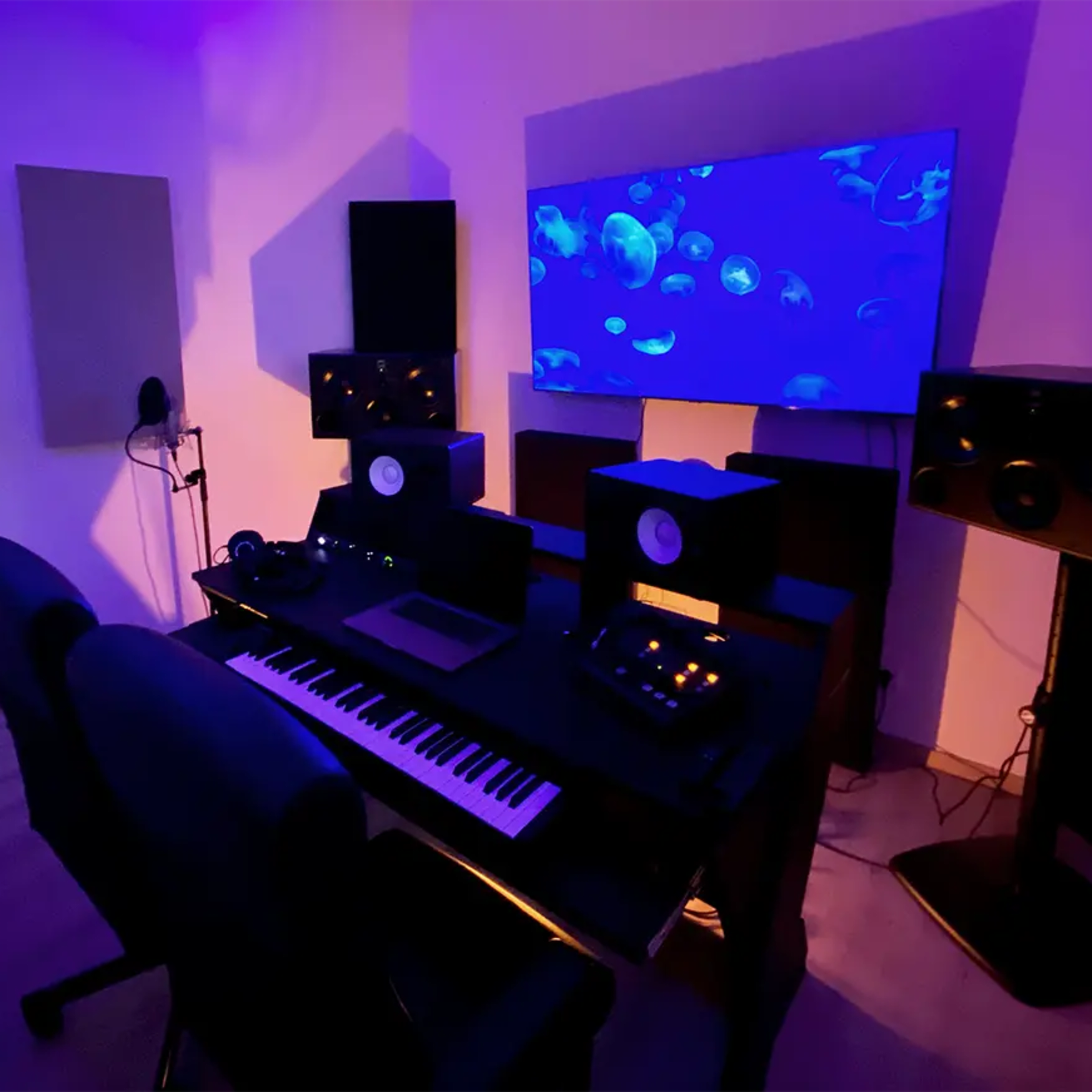 A music studio with a keyboard, audio monitors, and a large screen displaying an animated underwater scene.