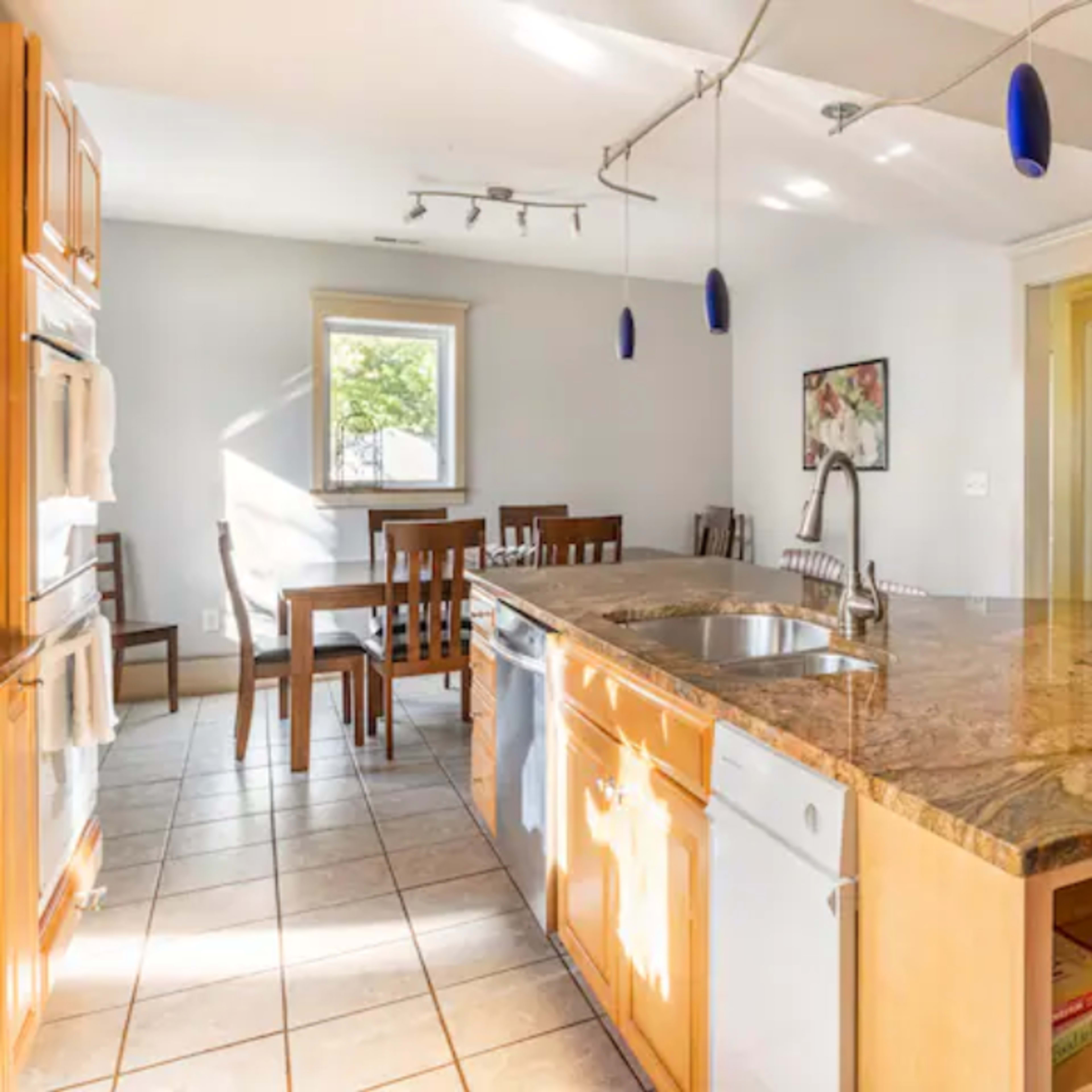 A kitchen features wooden cabinets, a granite countertop island with a sink, and a dining area with a table and chairs.