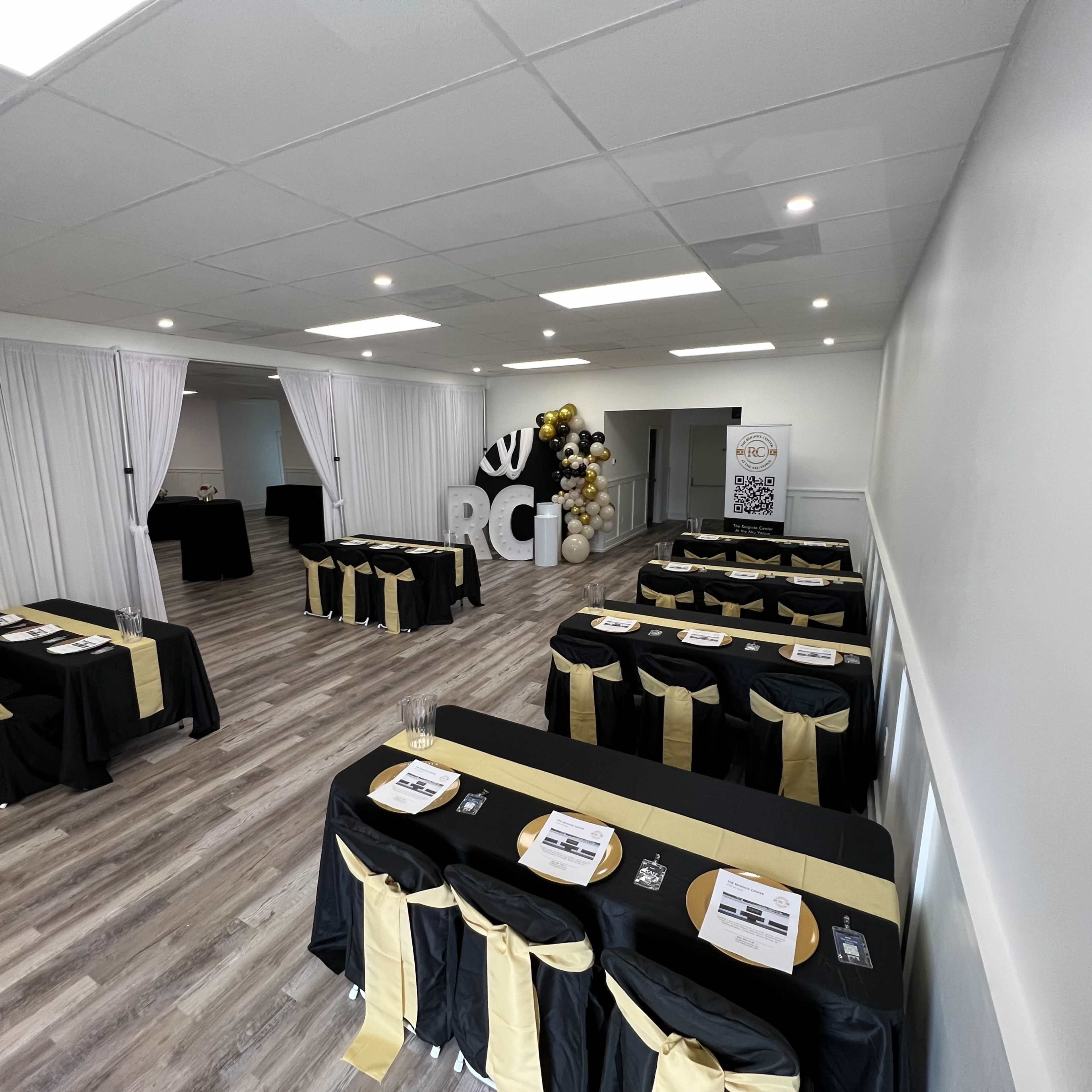 The room features multiple tables dressed in black and gold, arranged for an event, with decorative elements and a large "RCI" sign in the background.