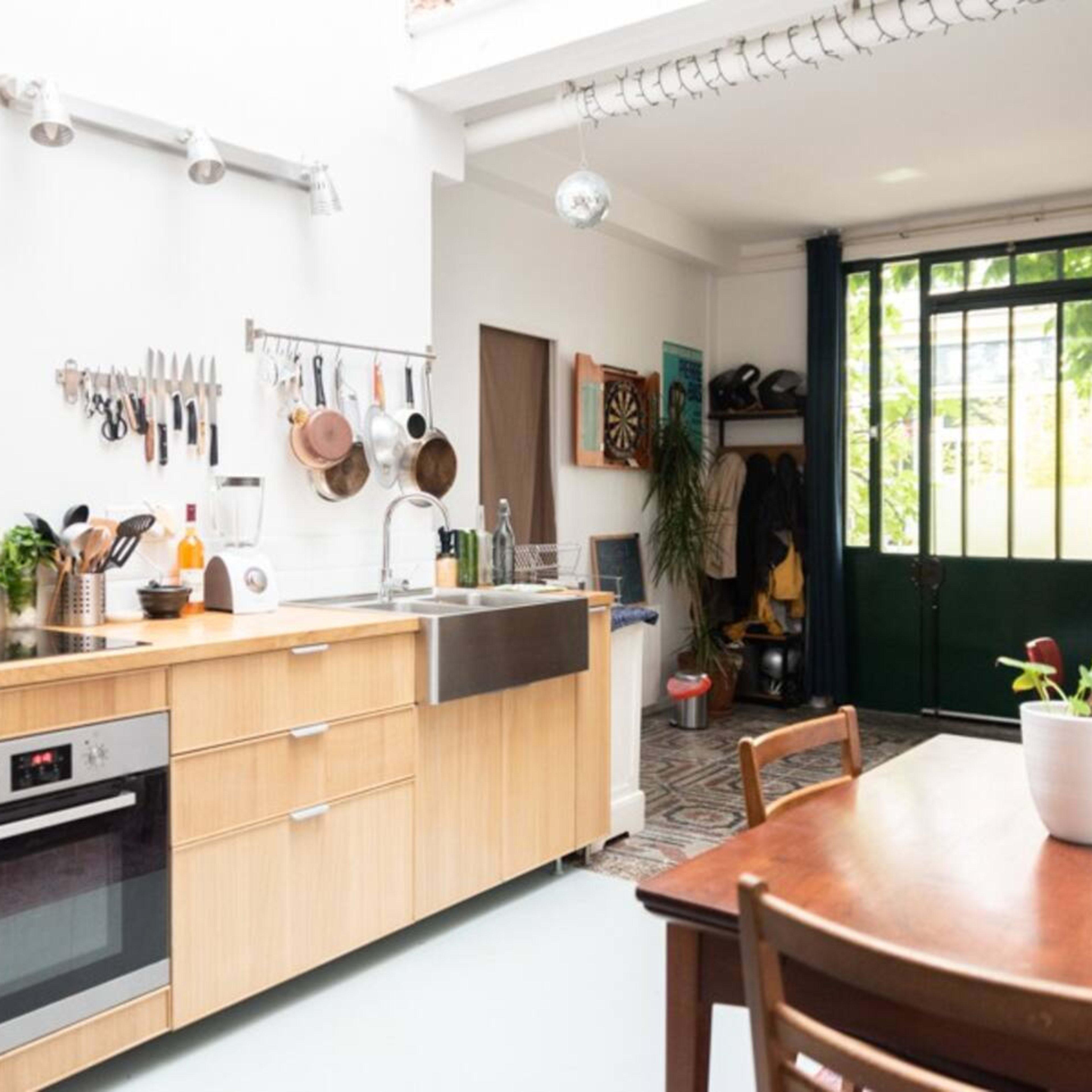 A modern kitchen with wooden cabinetry, a stainless steel sink, and a view of an outdoor area through a glass door.