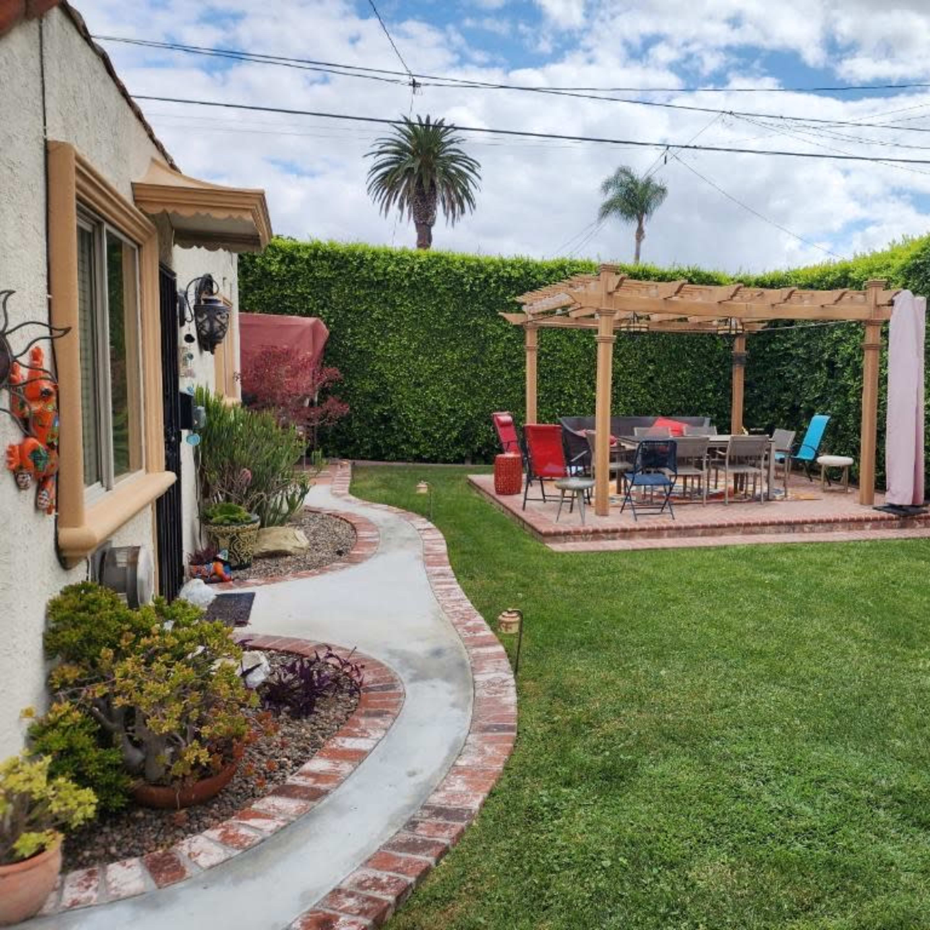 A backyard with a wooden pergola over a dining area surrounded by well-manicured grass and hedges.