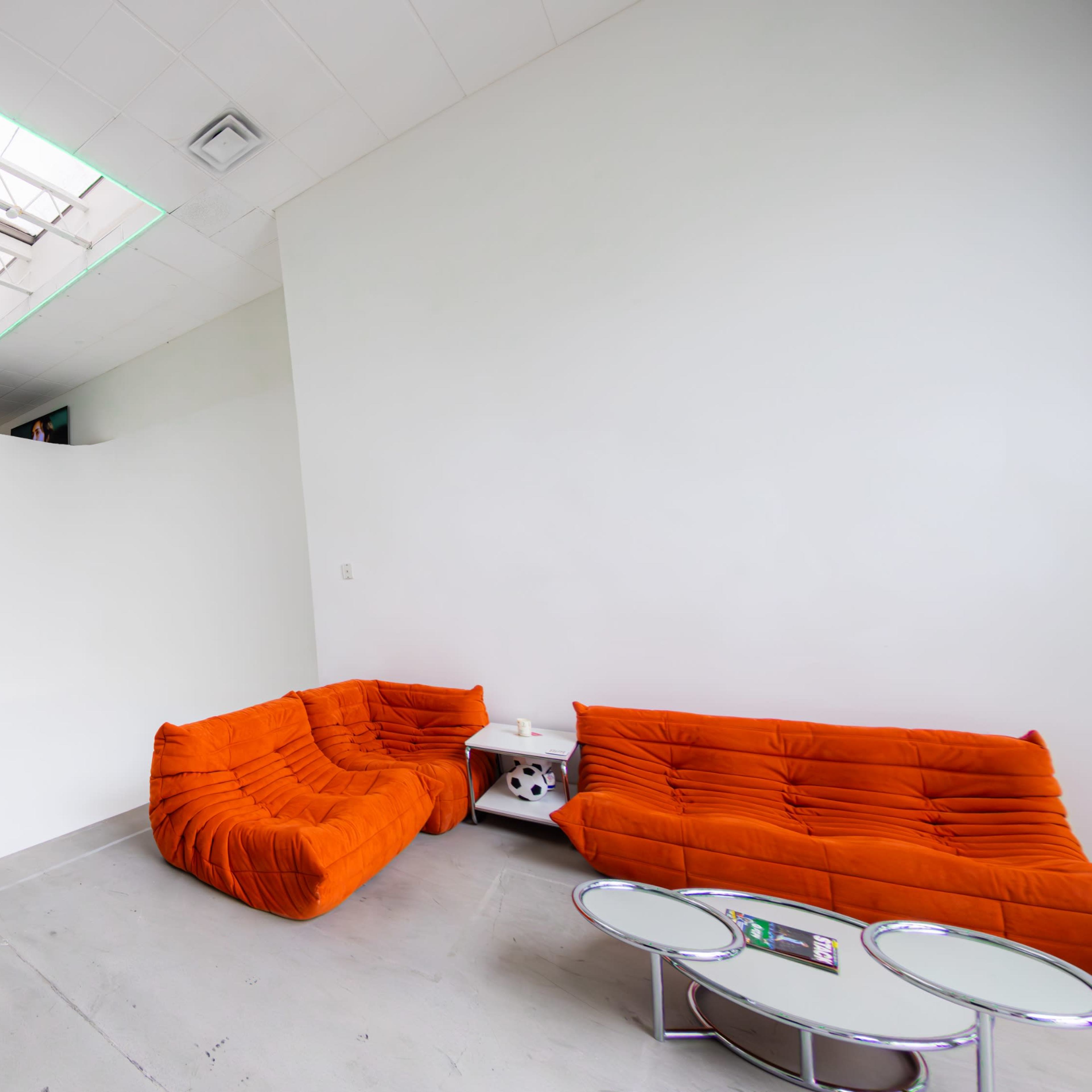 A modern interior with white walls, concrete flooring, orange sofas, and a skylight providing natural light.