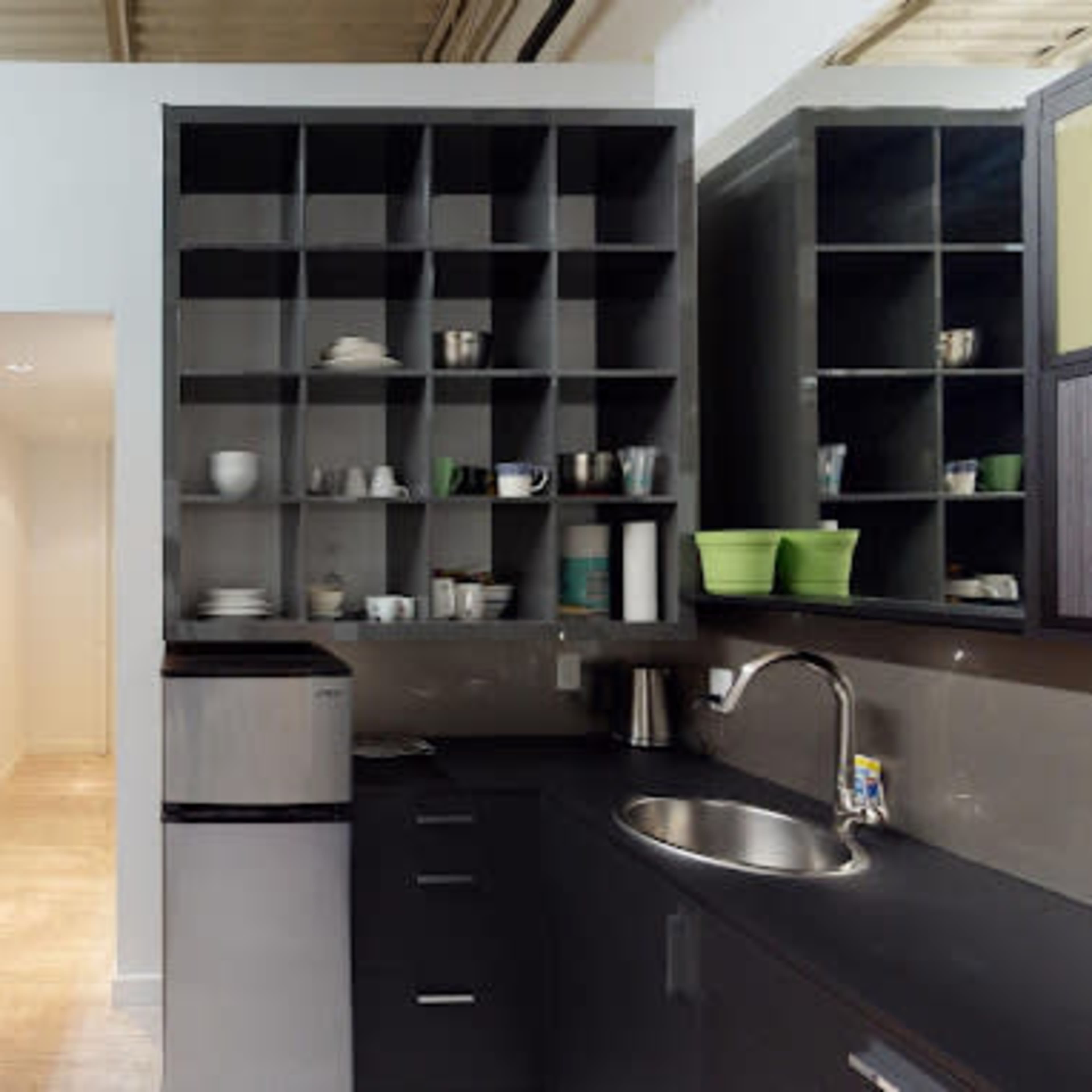 A modern kitchen area featuring cabinets, a sink, and countertop appliances, with a hallway visible in the background.