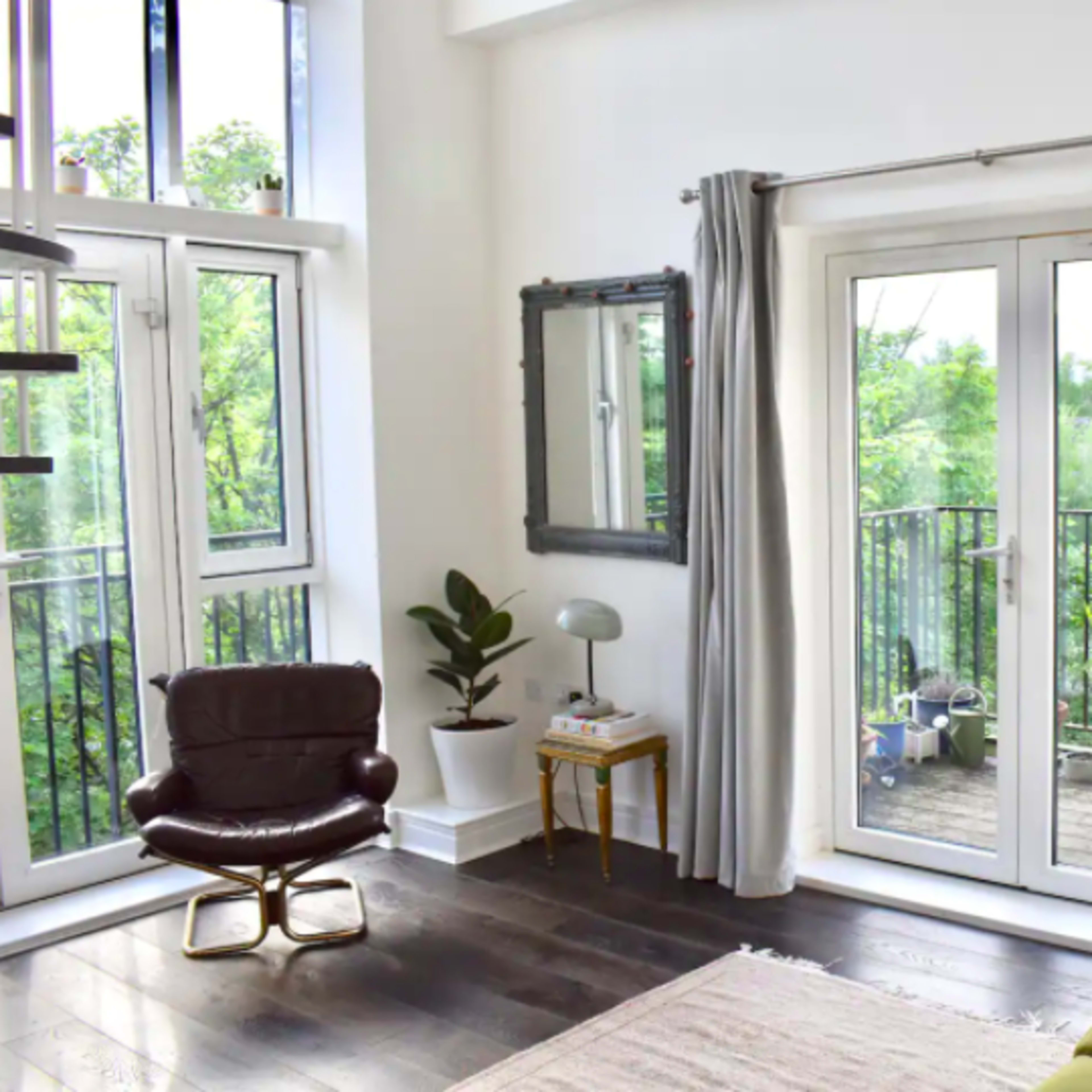A living room features a green sofa, a brown chair, and large glass doors leading to a balcony surrounded by greenery.
