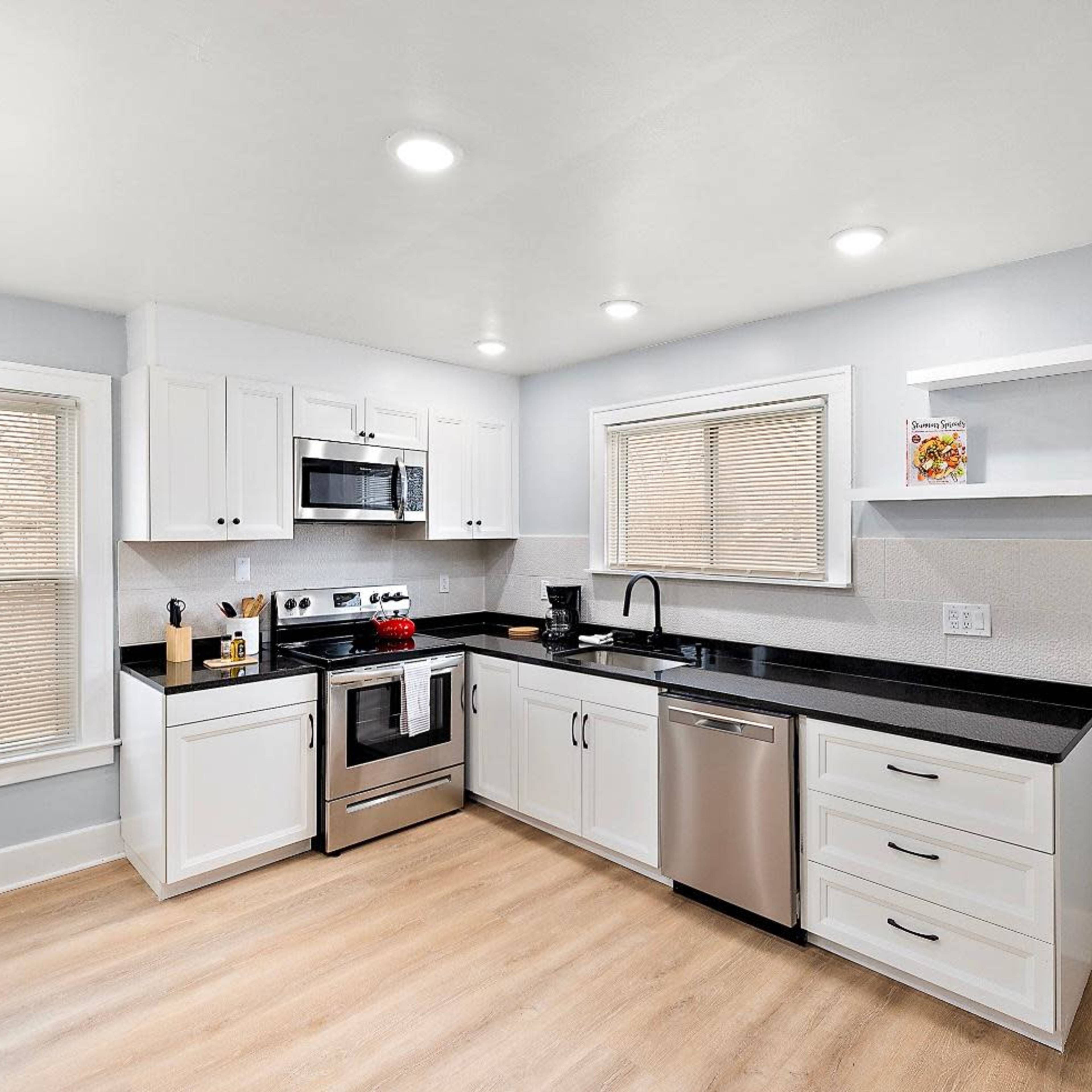 A modern kitchen features white cabinetry, stainless steel appliances, and a black countertop with wood-style flooring.