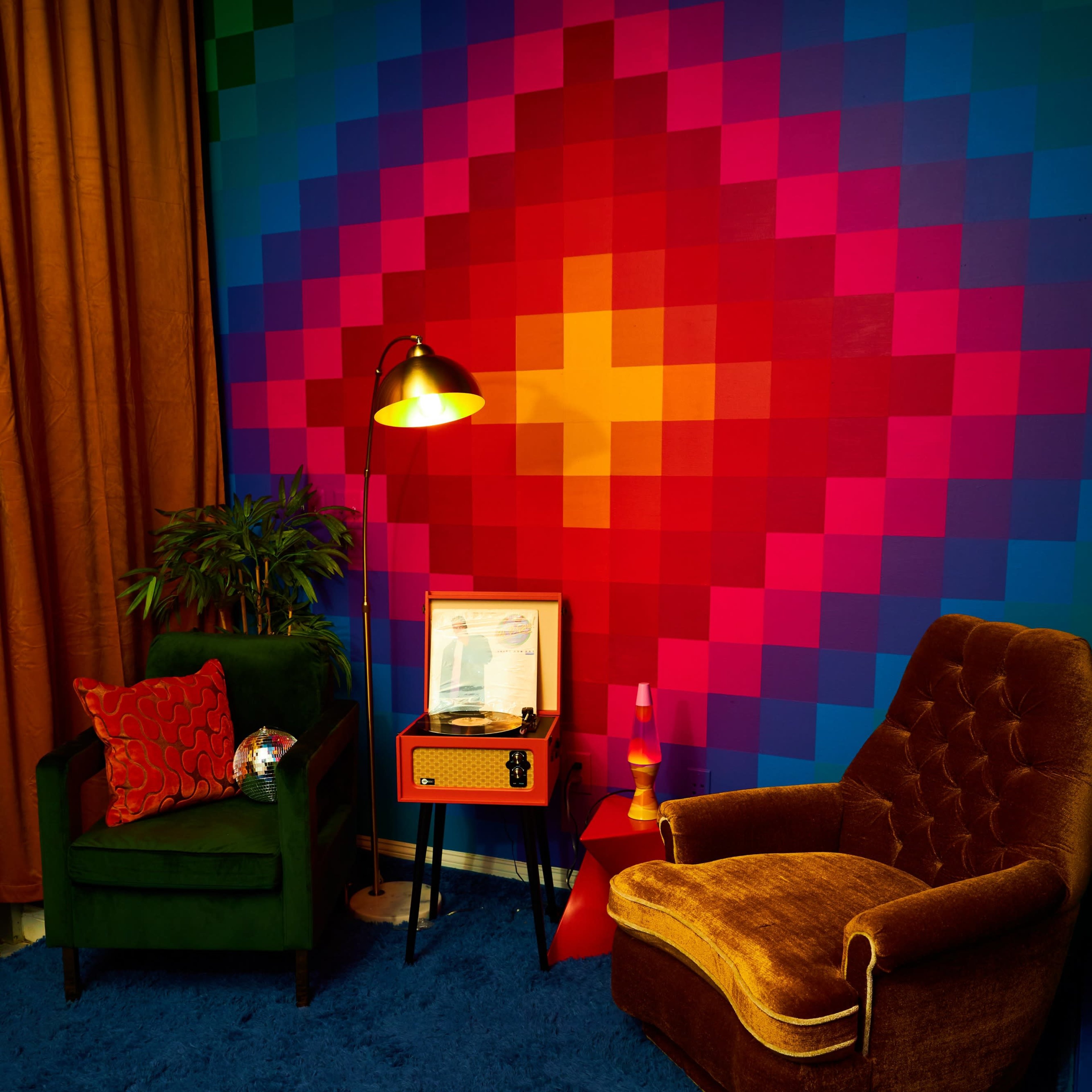 A colorful living space featuring two chairs, a lamp, a coffee table, and a patterned wall with vibrant squares.