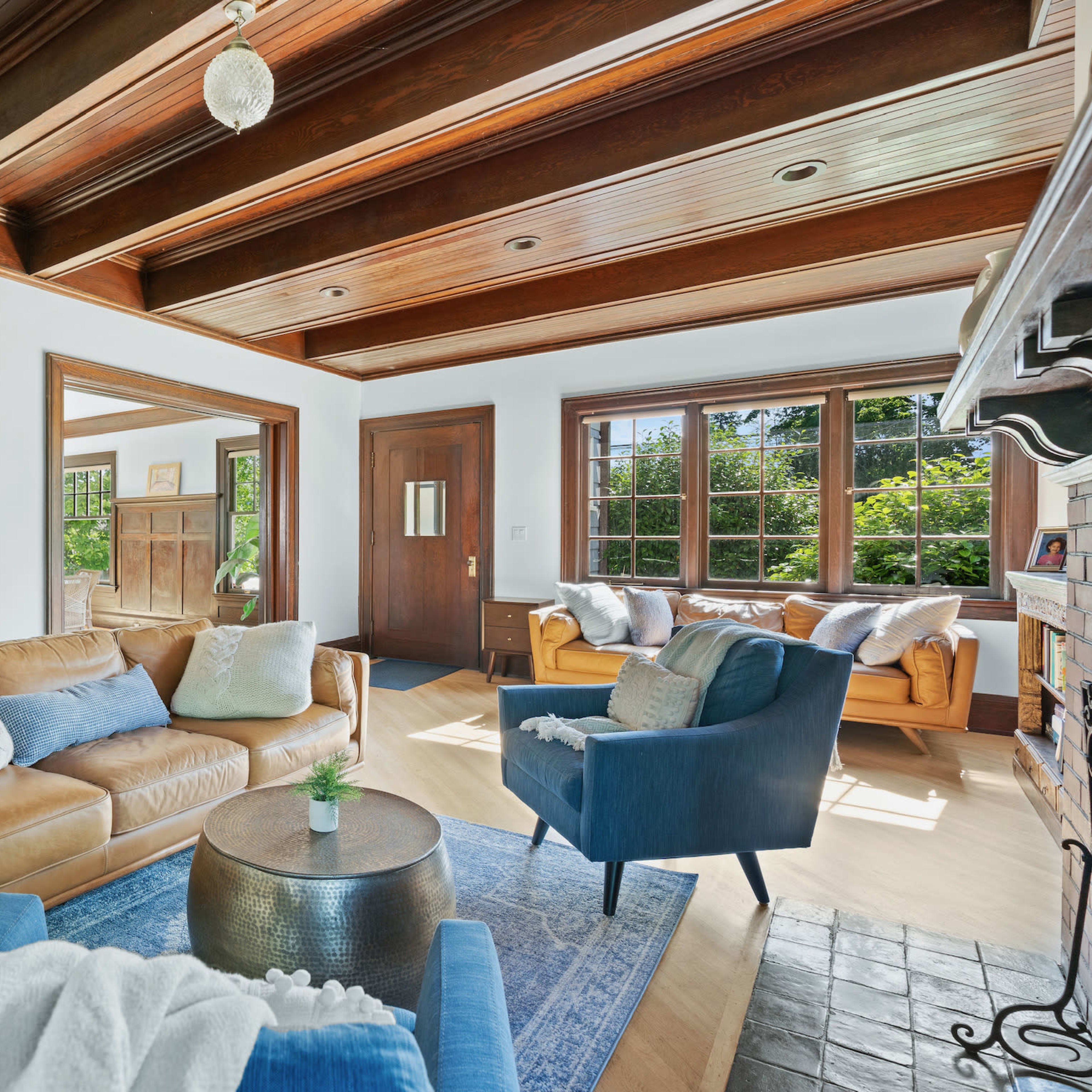 The living room features a mix of seating options, including a brown leather sofa and blue armchairs, with large windows allowing natural light to fill the space.