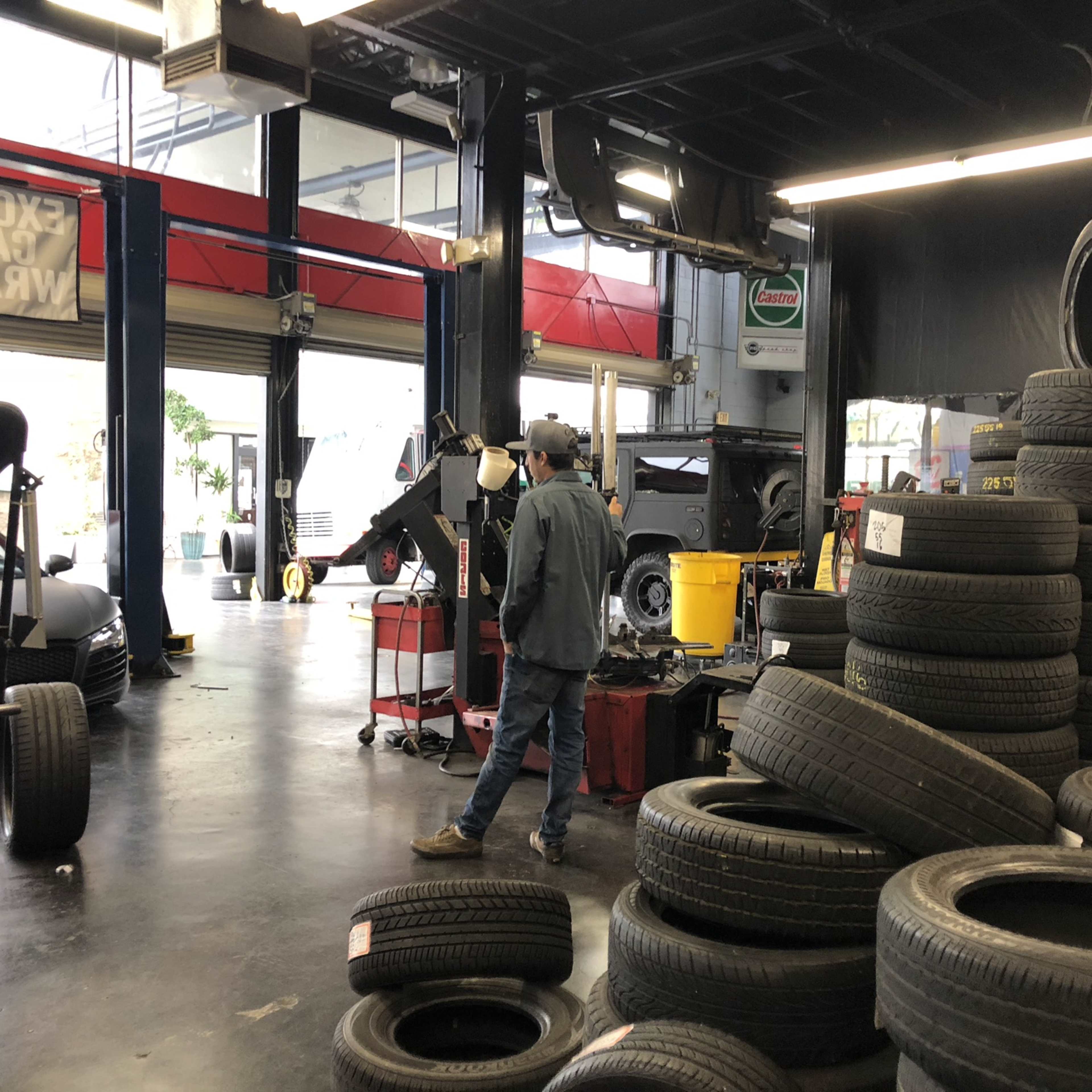 A mechanic walks past a stack of used tires in a bustling auto repair shop.