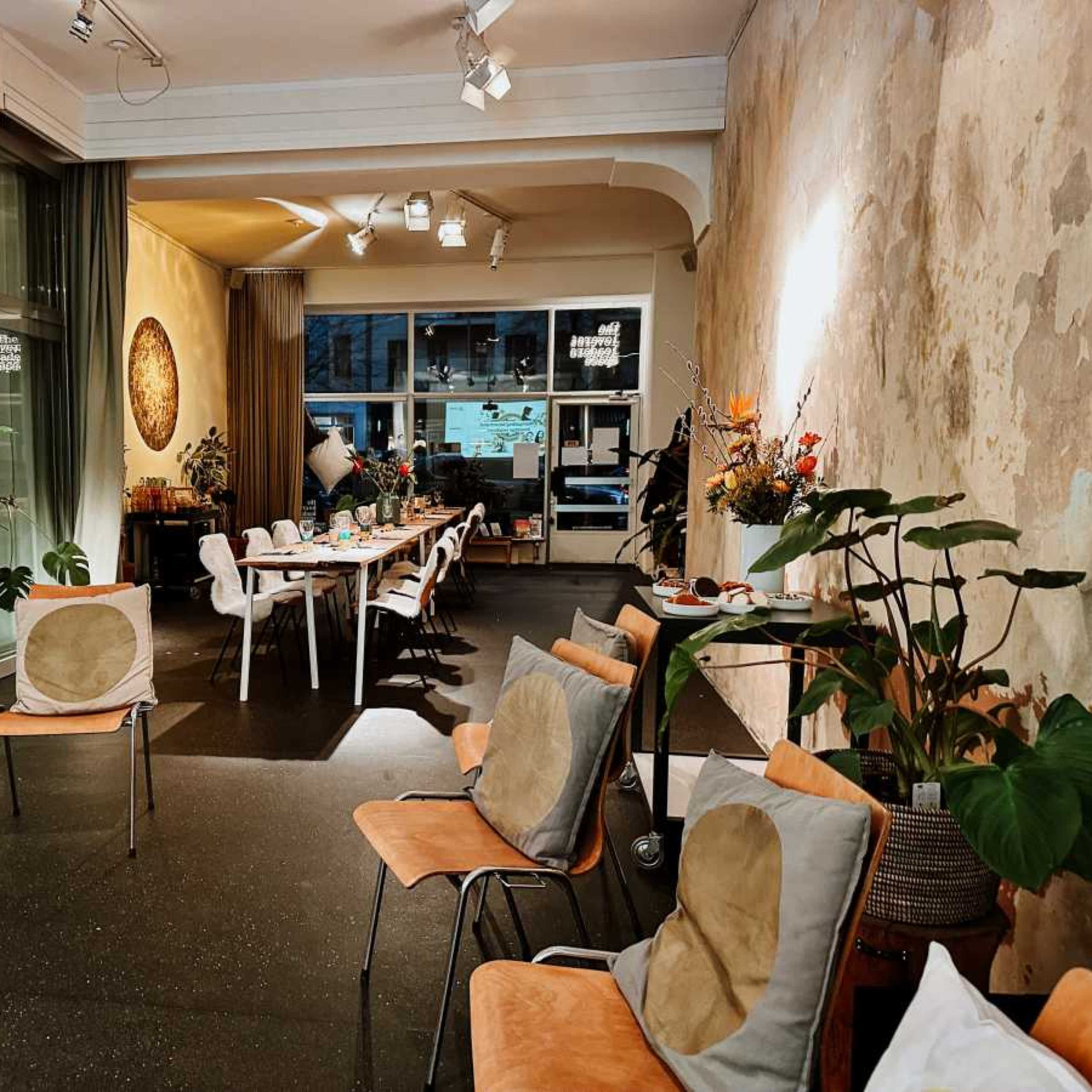 A spacious interior with chairs arranged around a long dining table, alongside decorative plants and textured walls.
