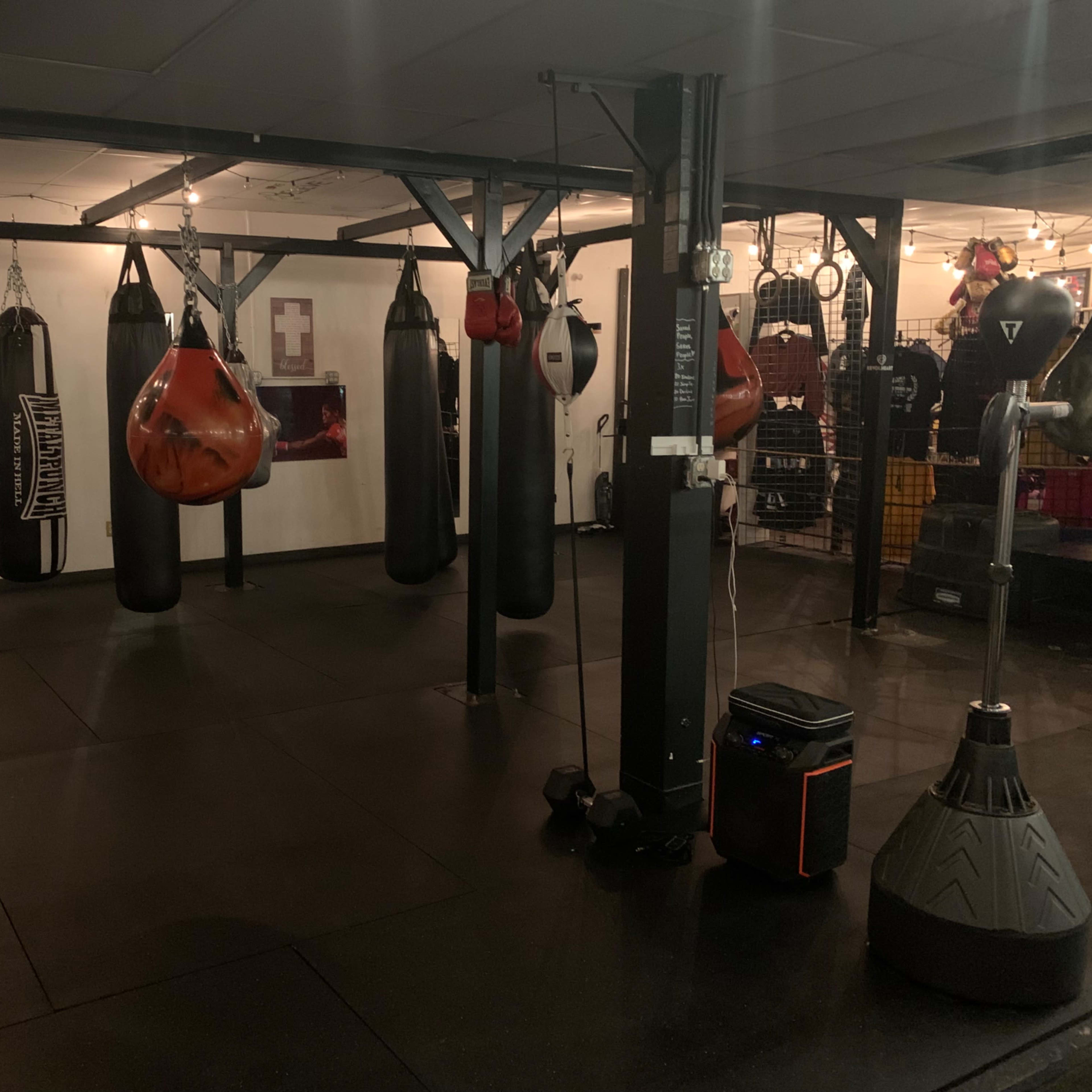 A boxing gym featuring several hanging punching bags and workout equipment in a dimly lit space.