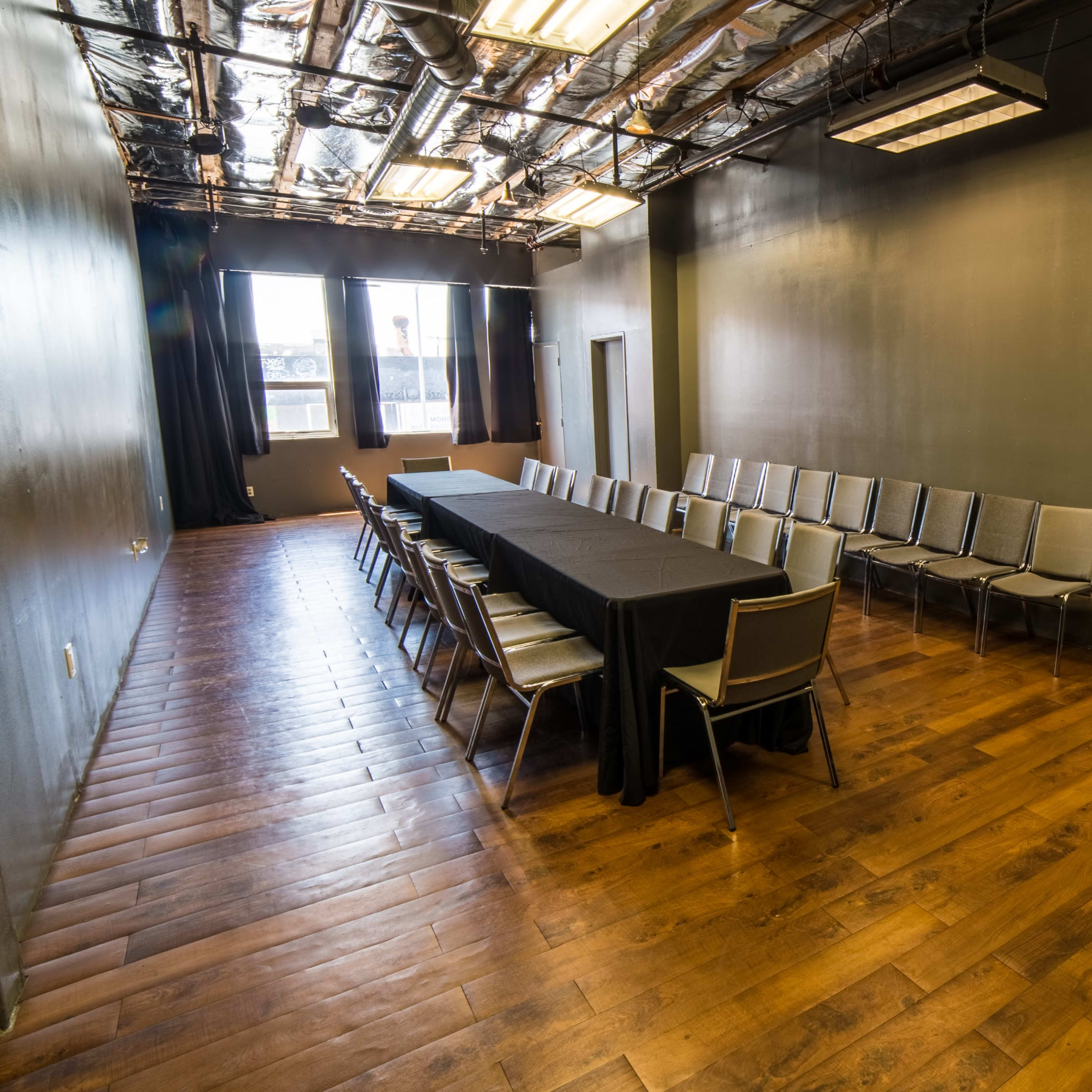 A long, rectangular conference room with a black tablecloth covering a table and rows of chairs along the walls, featuring wooden flooring and large windows providing natural light.