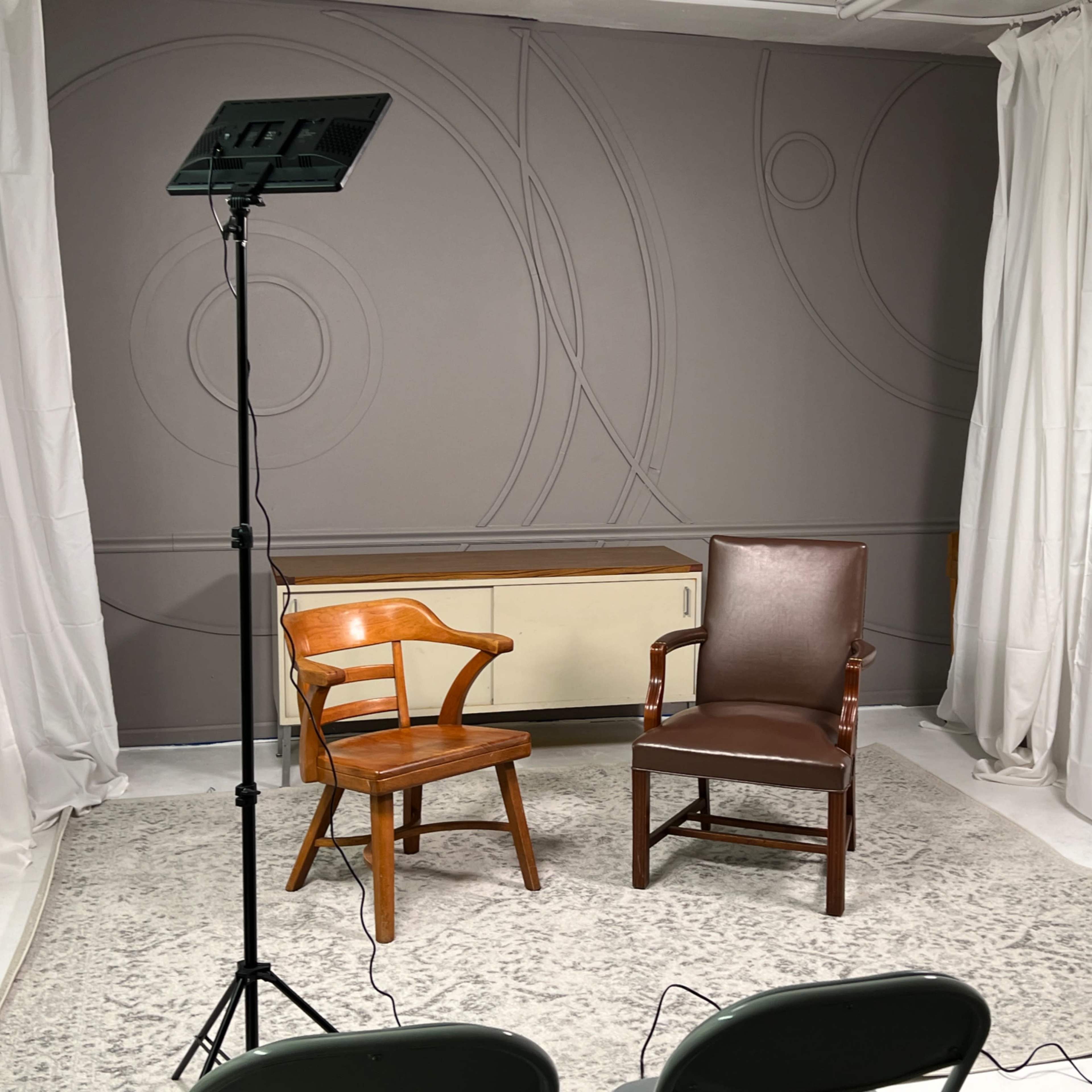 Two chairs positioned in a studio setting, with soft lighting and white curtains in the background.