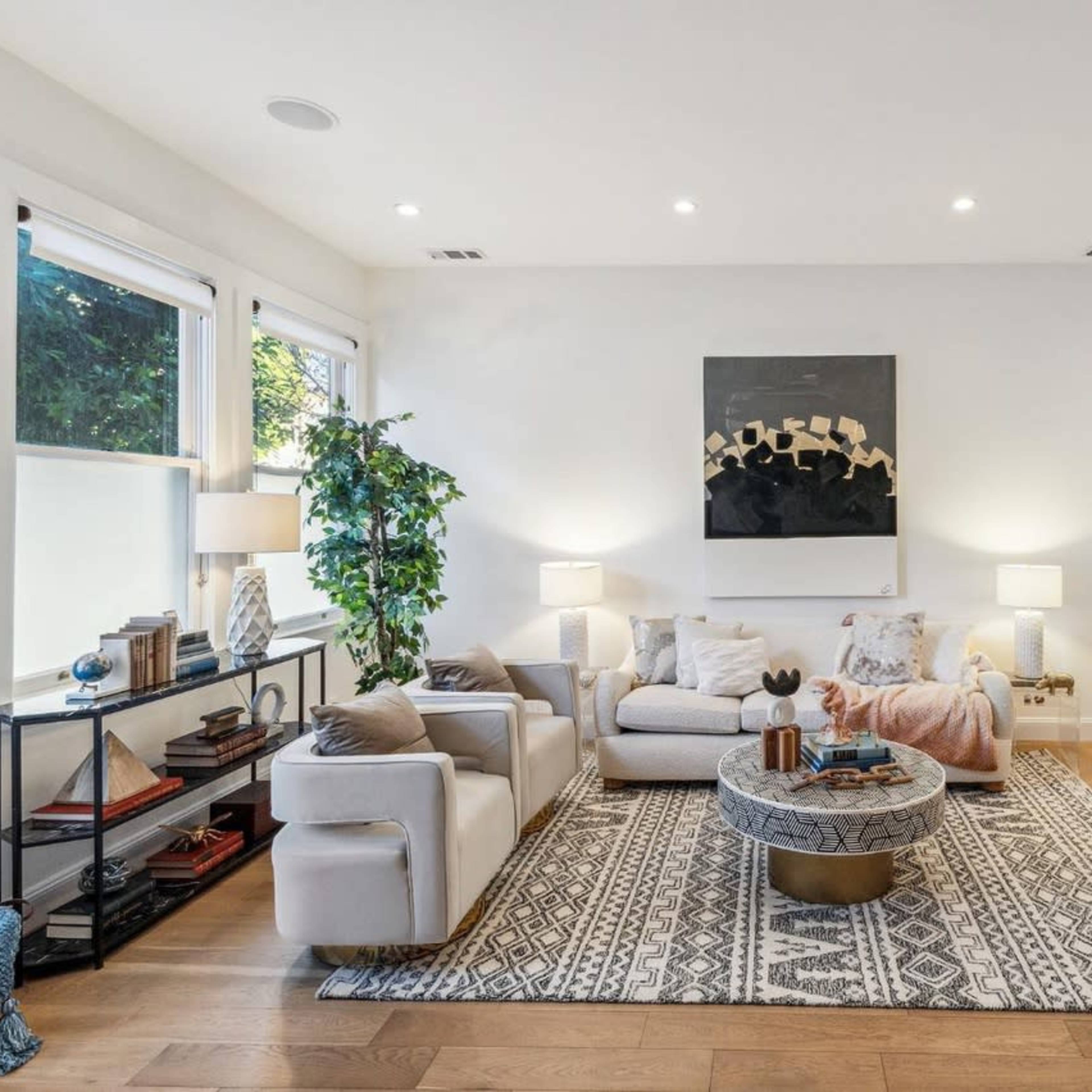 A modern living room with a neutral color palette, a large area rug, a round coffee table, and a dining area in the background.