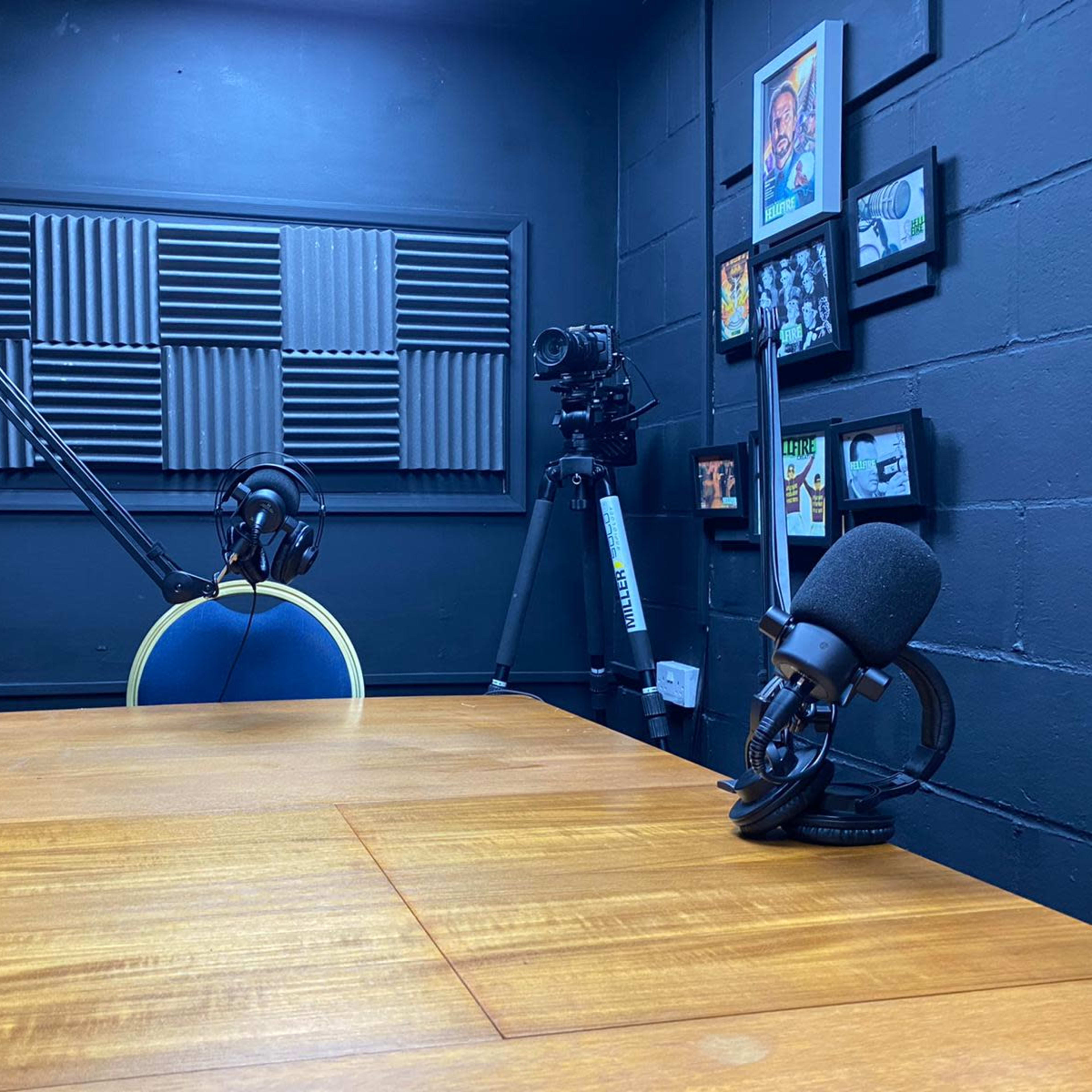 A recording studio with a wooden table, microphone setups, a chair, and wall-mounted soundproof panels.