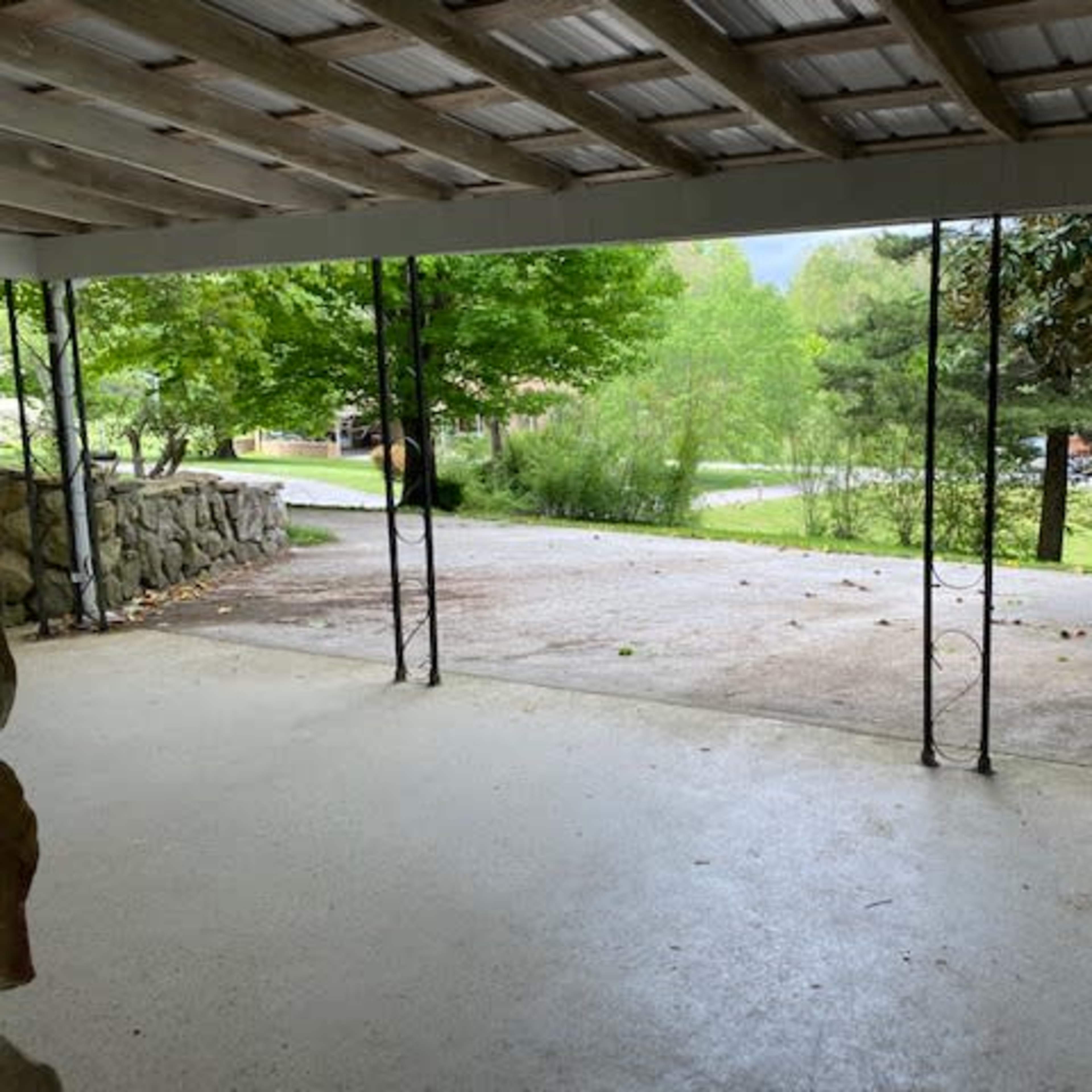 A covered porch reveals a concrete driveway leading through a park-like setting with trees in the background.