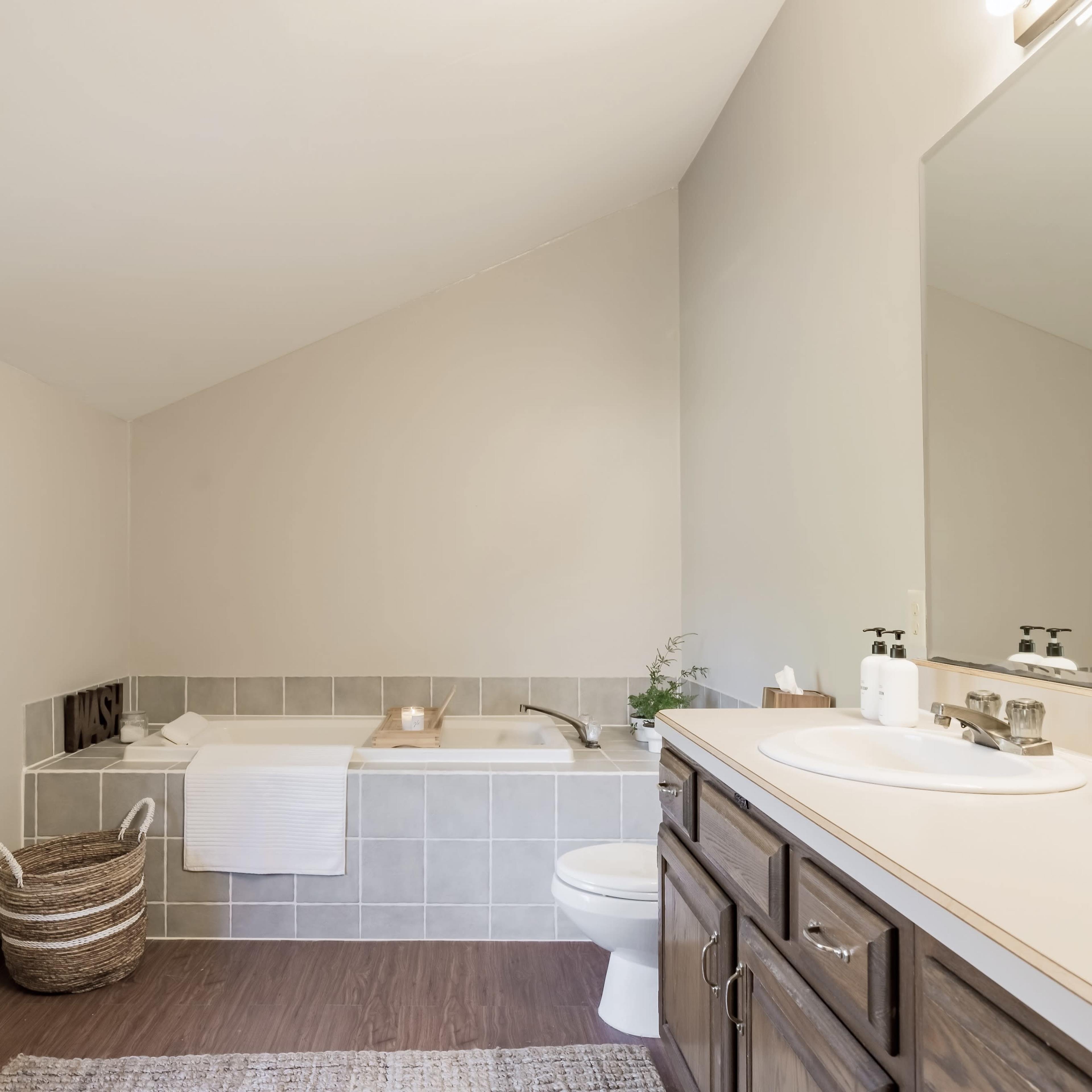 The bathroom features a bathtub beside a large window, a sink with a mirror above, and dark wood cabinetry.