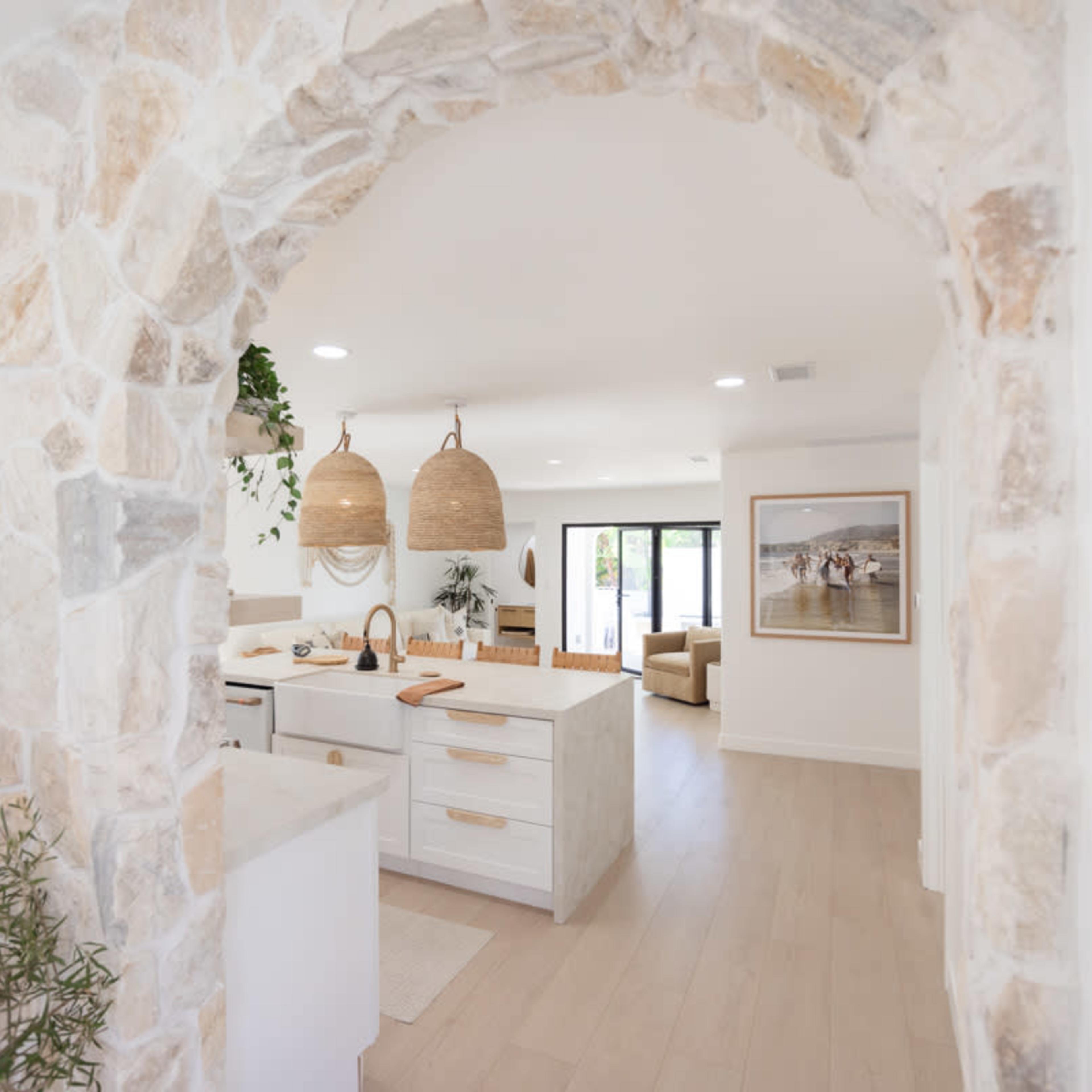 A view of a modern kitchen and living area framed by a stone archway.