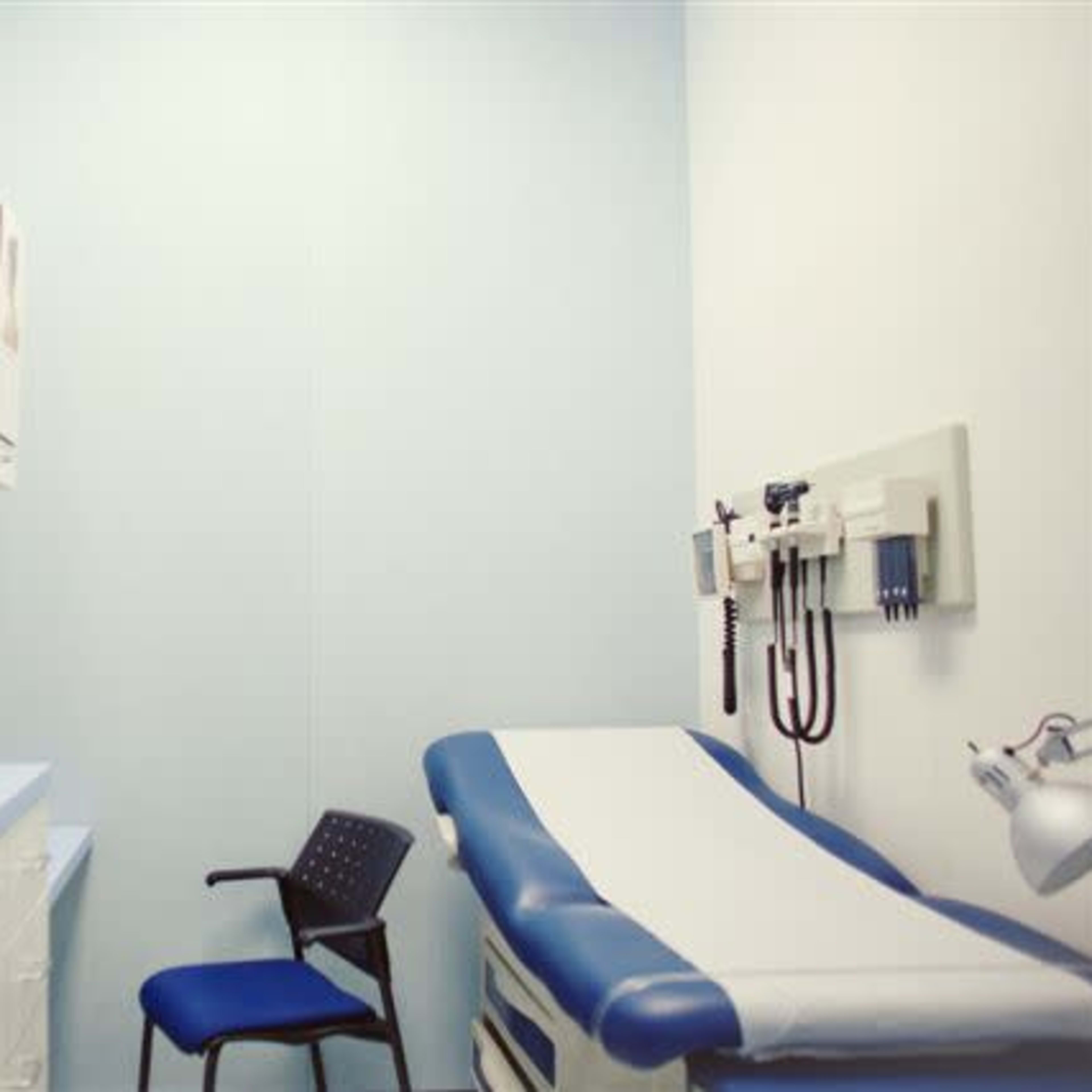A medical examination room featuring a blue examination table, a chair, and wall-mounted medical equipment.