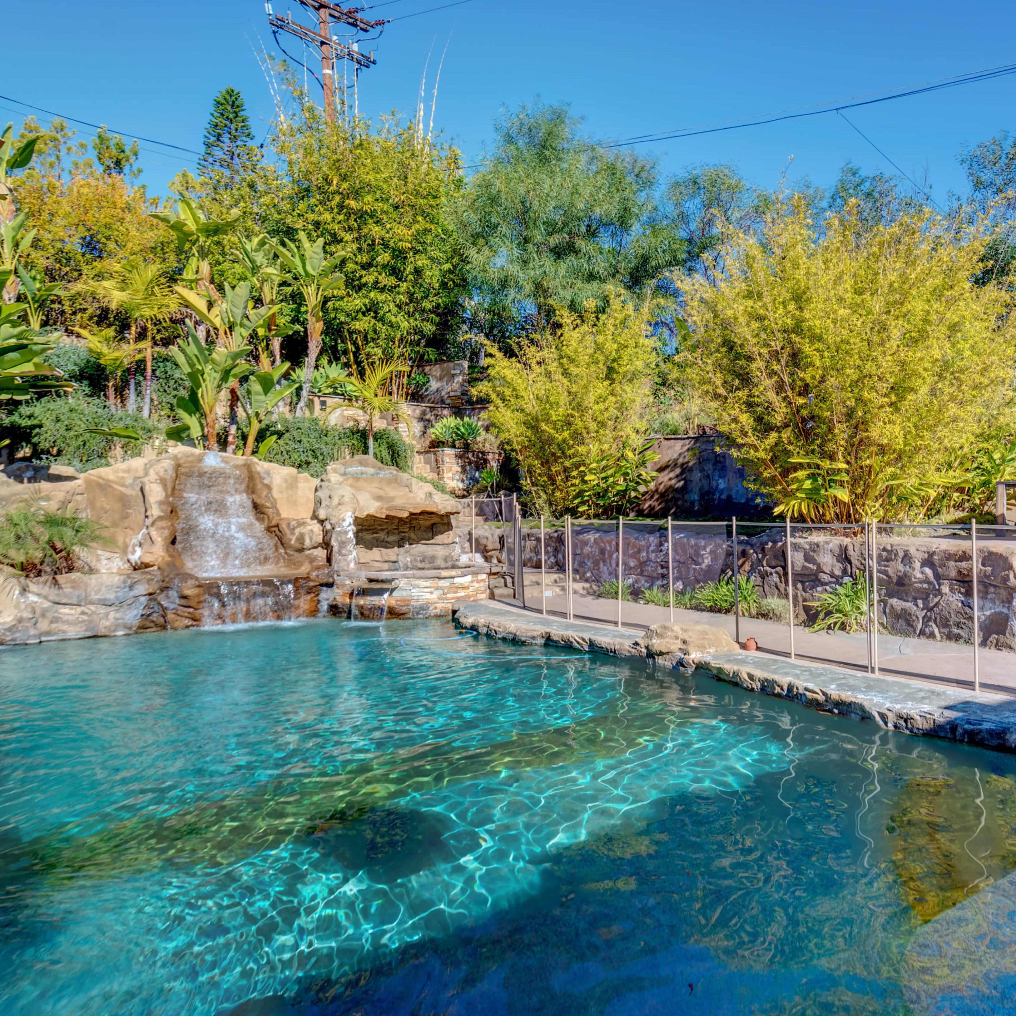A landscaped swimming pool area with a rock waterfall and surrounding lush greenery.