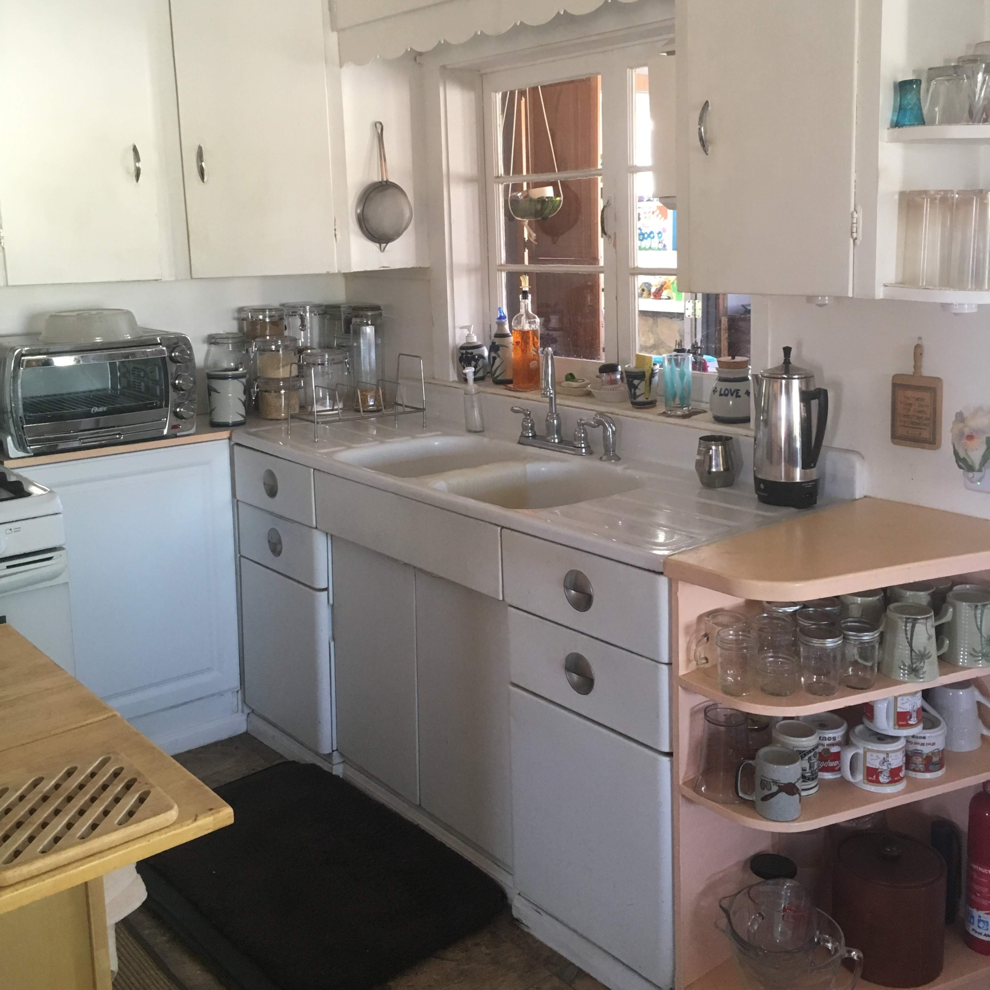 A tidy kitchen with white cabinets, a double sink, and various kitchen appliances, including a toaster and coffee maker, arranged neatly on the counter.