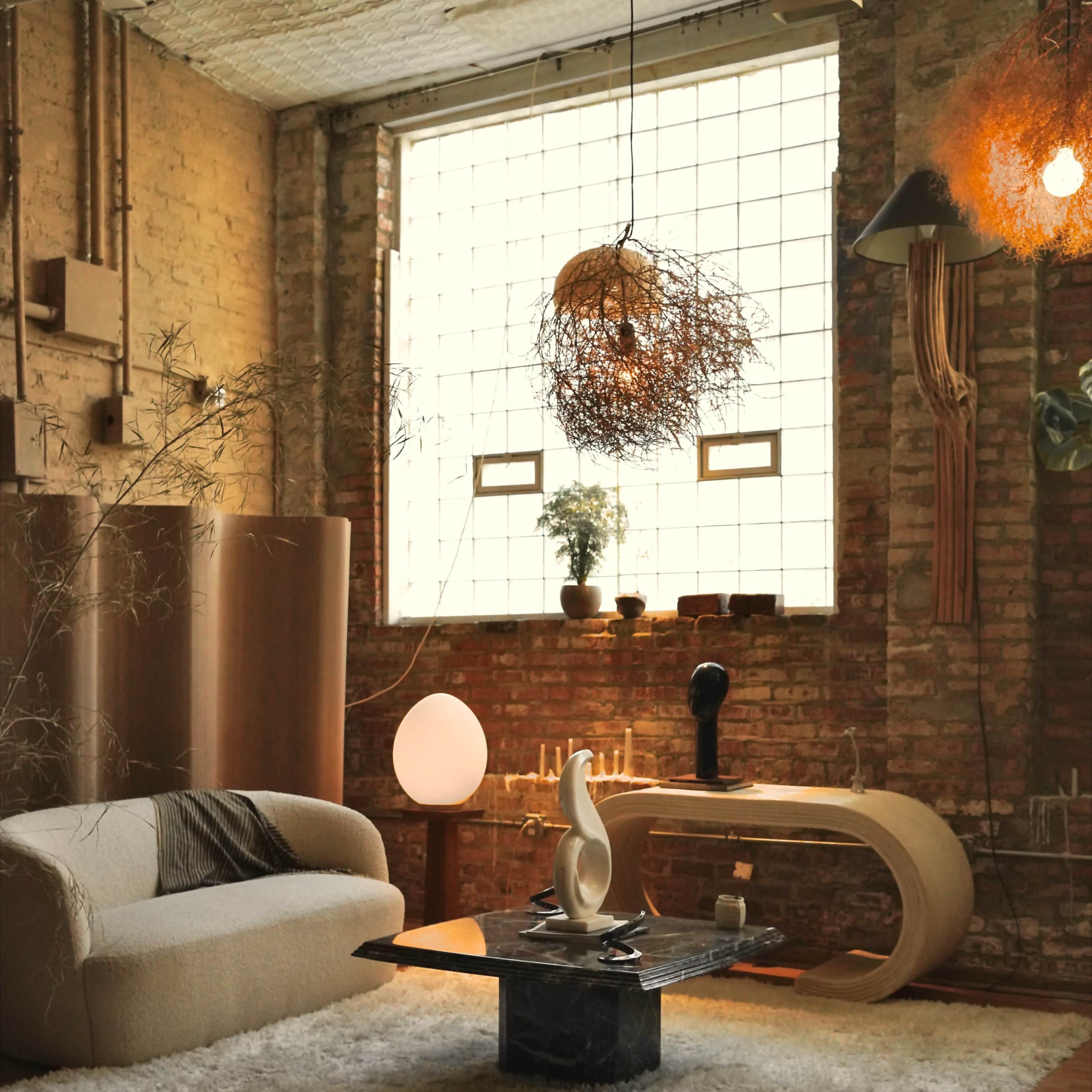 A cozy living room with a large window, a light-colored sofa, a curved wooden coffee table, and a textured rug on a wooden floor.